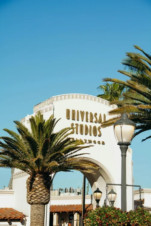 Large globe sculpture with the word 'UNIVERSAL' across it, located at Universal Studios theme park, with People and palm trees in the background.