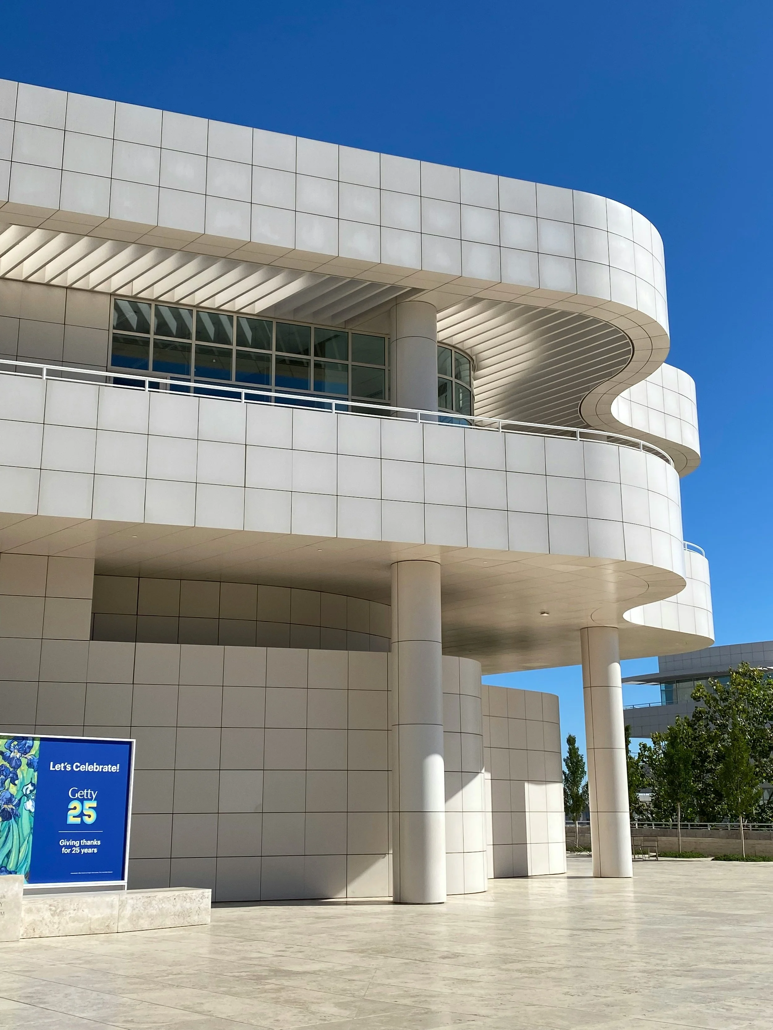 Modern white building with curved architecture, large windows, and a sign celebrating 25 years of Getty, with trees and a clear blue sky in the background.