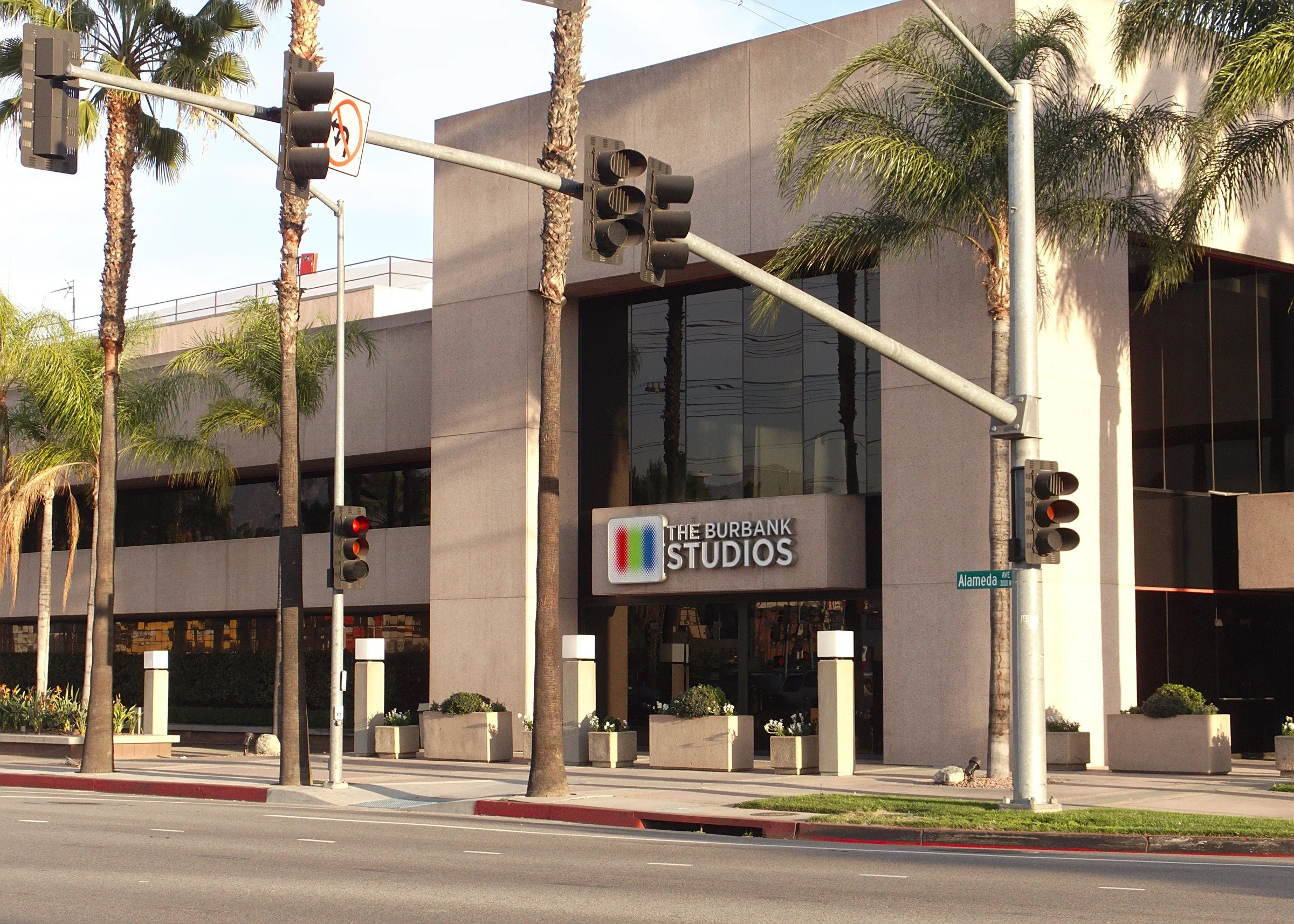 Exterior view of The Burbank Studios building with palm trees, street traffic lights, and a sign on the building, located at the corner of Alameda Avenue.