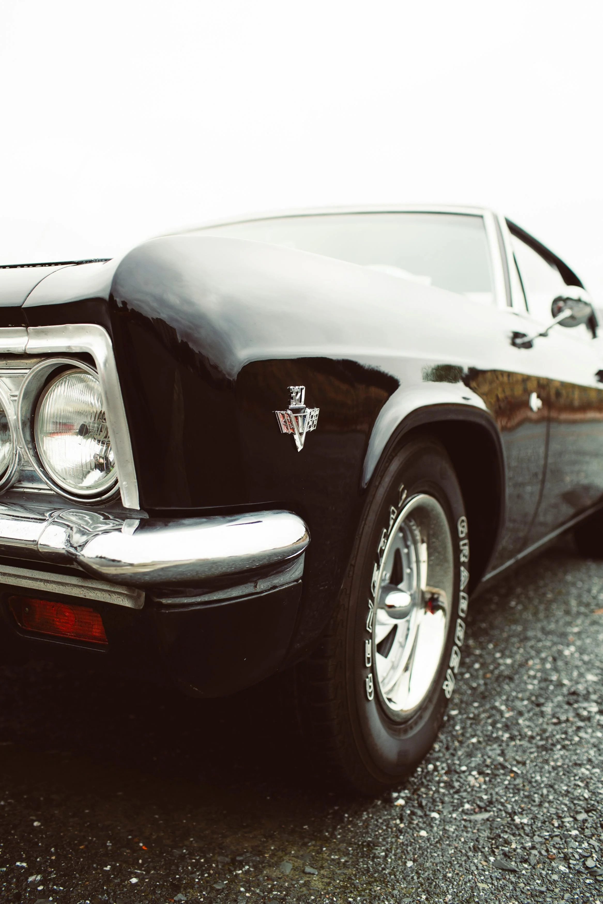Close-up of the front left side of a vintage black Pontiac Firebird with chrome accents, wrapped tires, and a glossy finish.