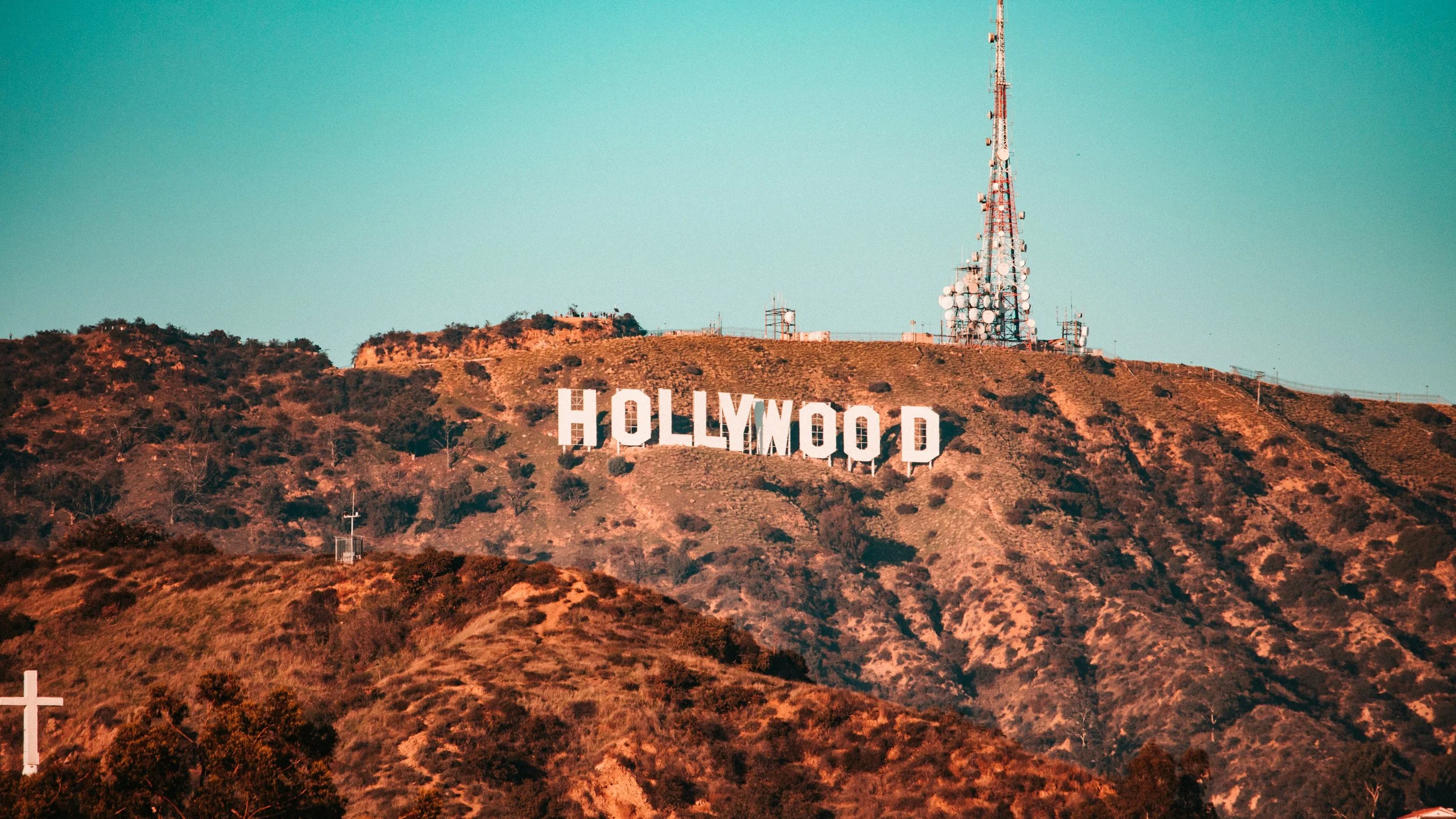 Hollywood sign on a hillside with radio antennas and a cross in the foreground.