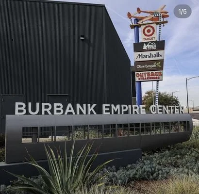 Sign for Burbank Empire Center shopping mall with stores listed, including Target, Miele, Marshalls, Celia G. Calendar, and Outback Steakhouse, against a cloudy sky.