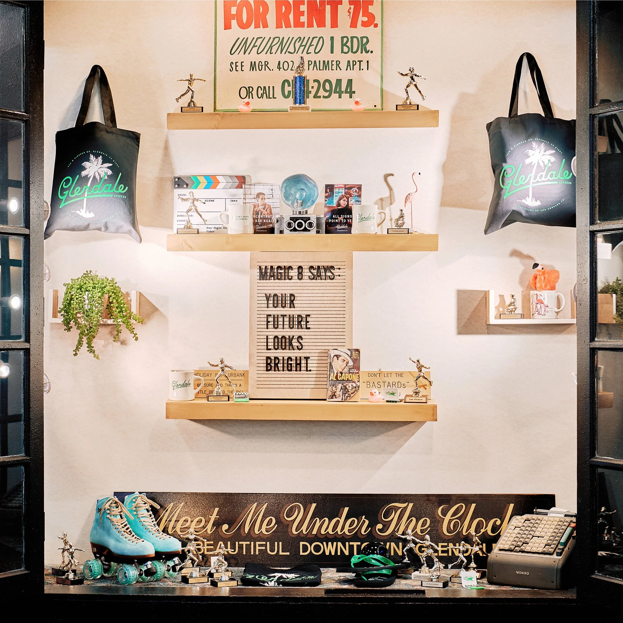 Decorative display window with roller skates, trophies, and various memorabilia, along with a sign that reads 'Meet Me Under The Clock' and a quote on a letter board that says 'Magic 8 Says: Your Future Looks Bright.'