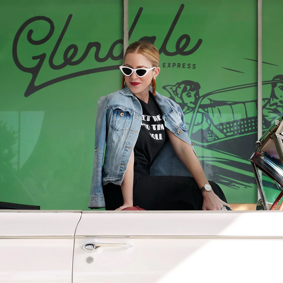 Woman with red hair wearing white sunglasses, denim jacket, black t-shirt, sitting on a white classic car in front of a green background with 'Glerdle' and illustration of a shopping cart.