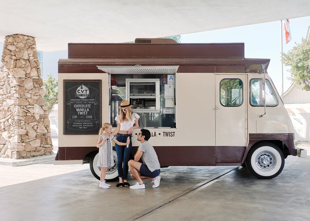 Family ordering ice cream from a vintage food truck under a concrete canopy.