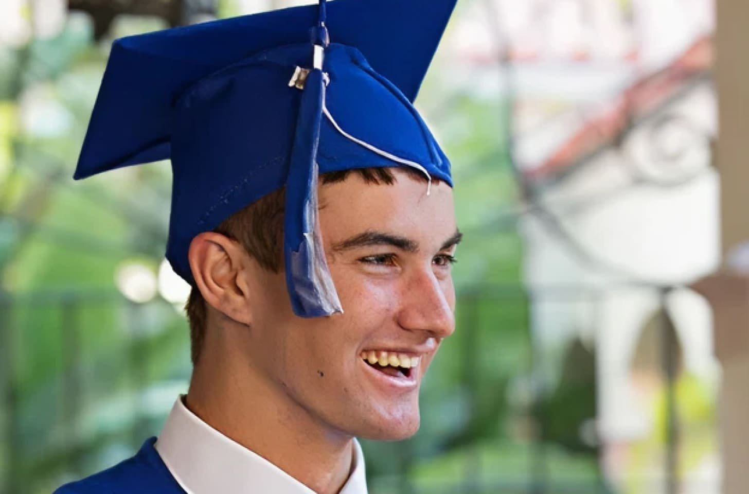 A young man in graduation cap smiling indoors.