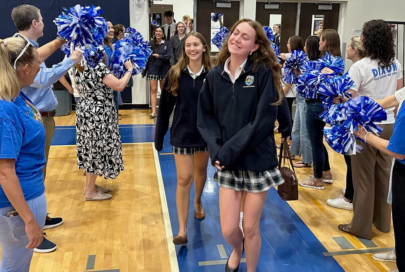 Students walking through a hallway lined with cheerleaders holding blue and white pom-poms, creating a celebratory atmosphere.