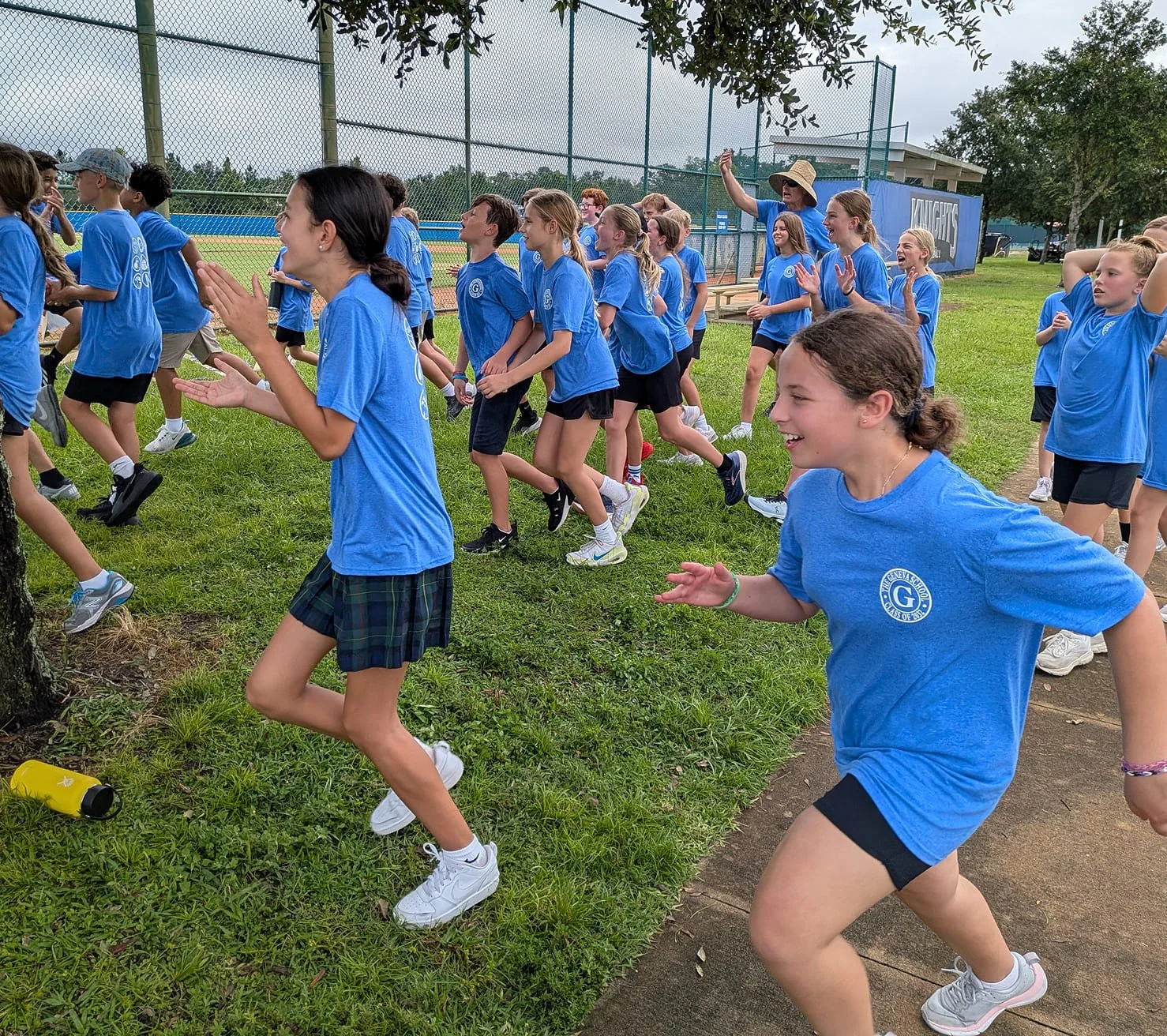 A group of children in blue T-shirts participating in an outdoor race or running event on a grassy field.