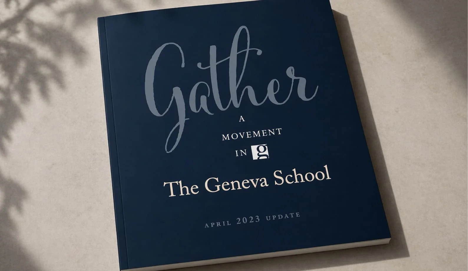 Book titled "Gather: A Movement in the Geneva School" with a subtitle "April 2023 Update," placed on a light surface with shadows of leaves.