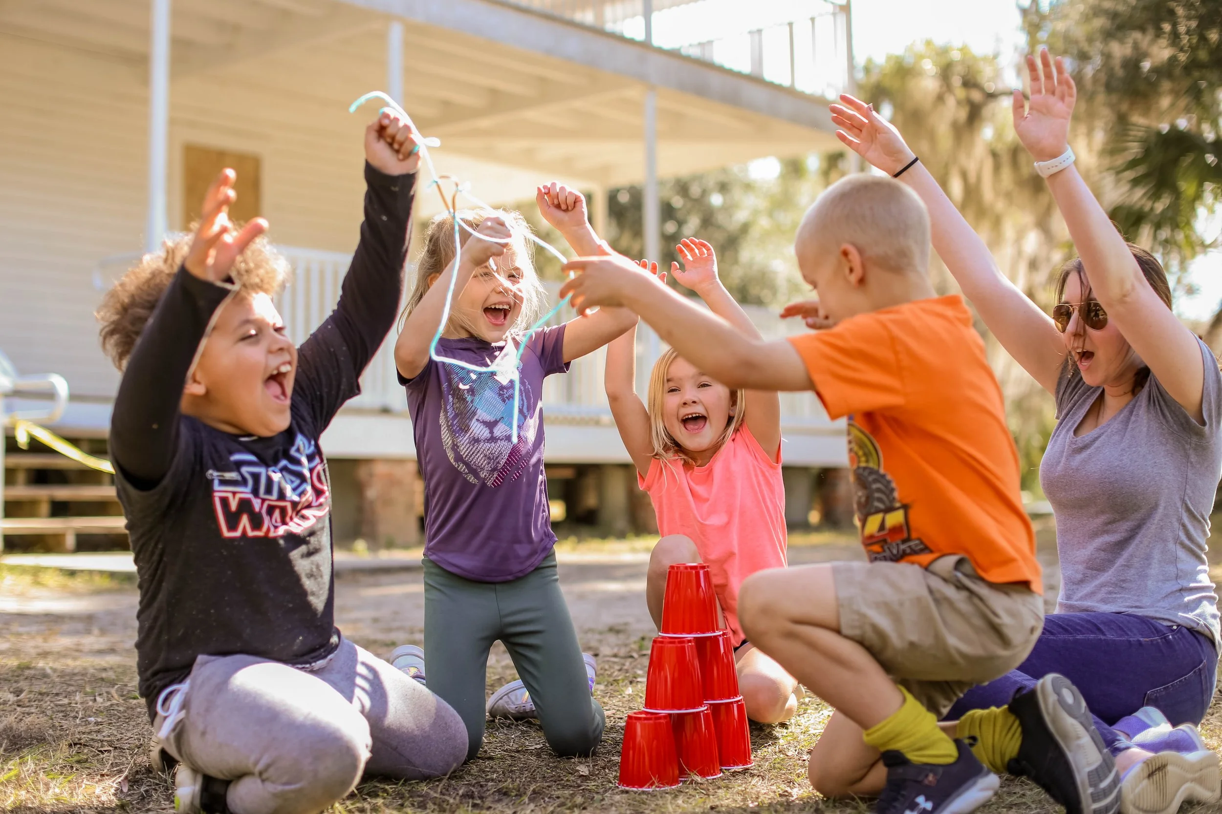 Group of children playing outdoors, stacking red plastic cups, happy and excited.