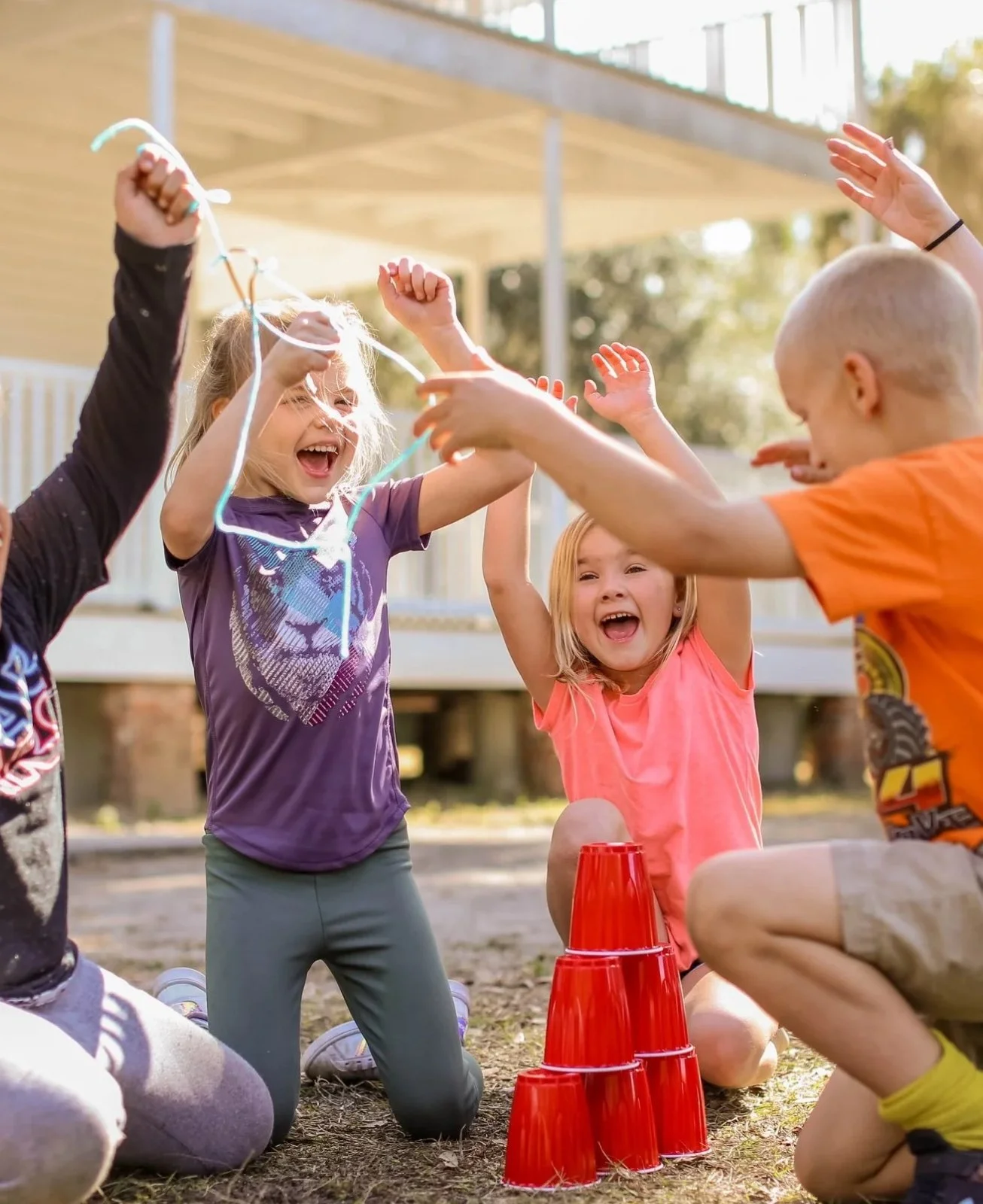 Children playing outdoors with red stacking cups and a blue jump rope, smiling and having fun.