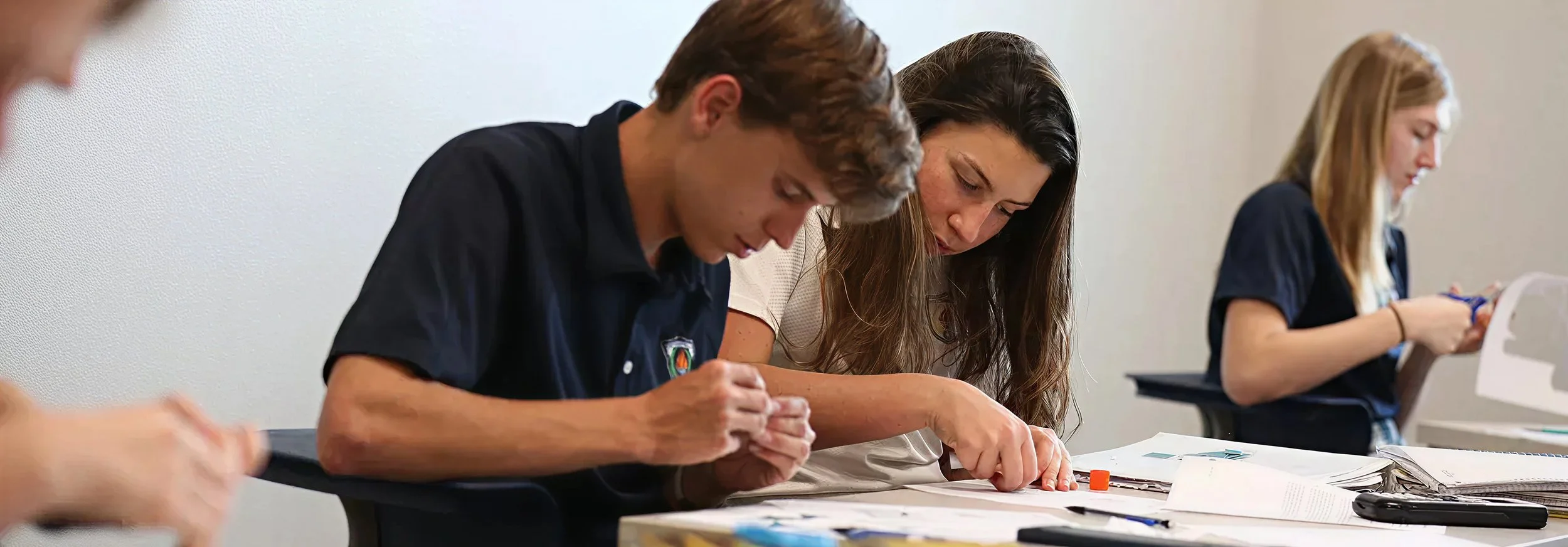 Group of students sitting at desks, focused on their work, with books and papers on the table.