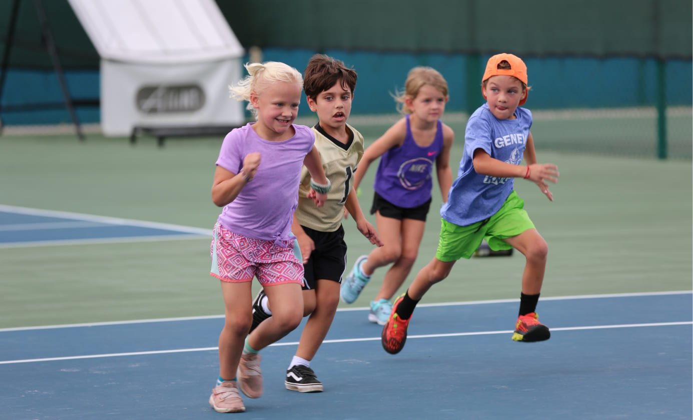 Four children running on a tennis court during daytime.