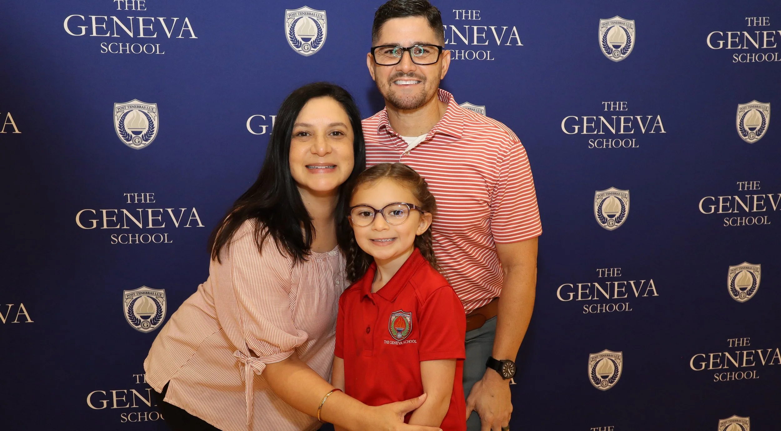 Family standing in front of a blue backdrop with 'The Geneva School' logo and text, posing for a photo.