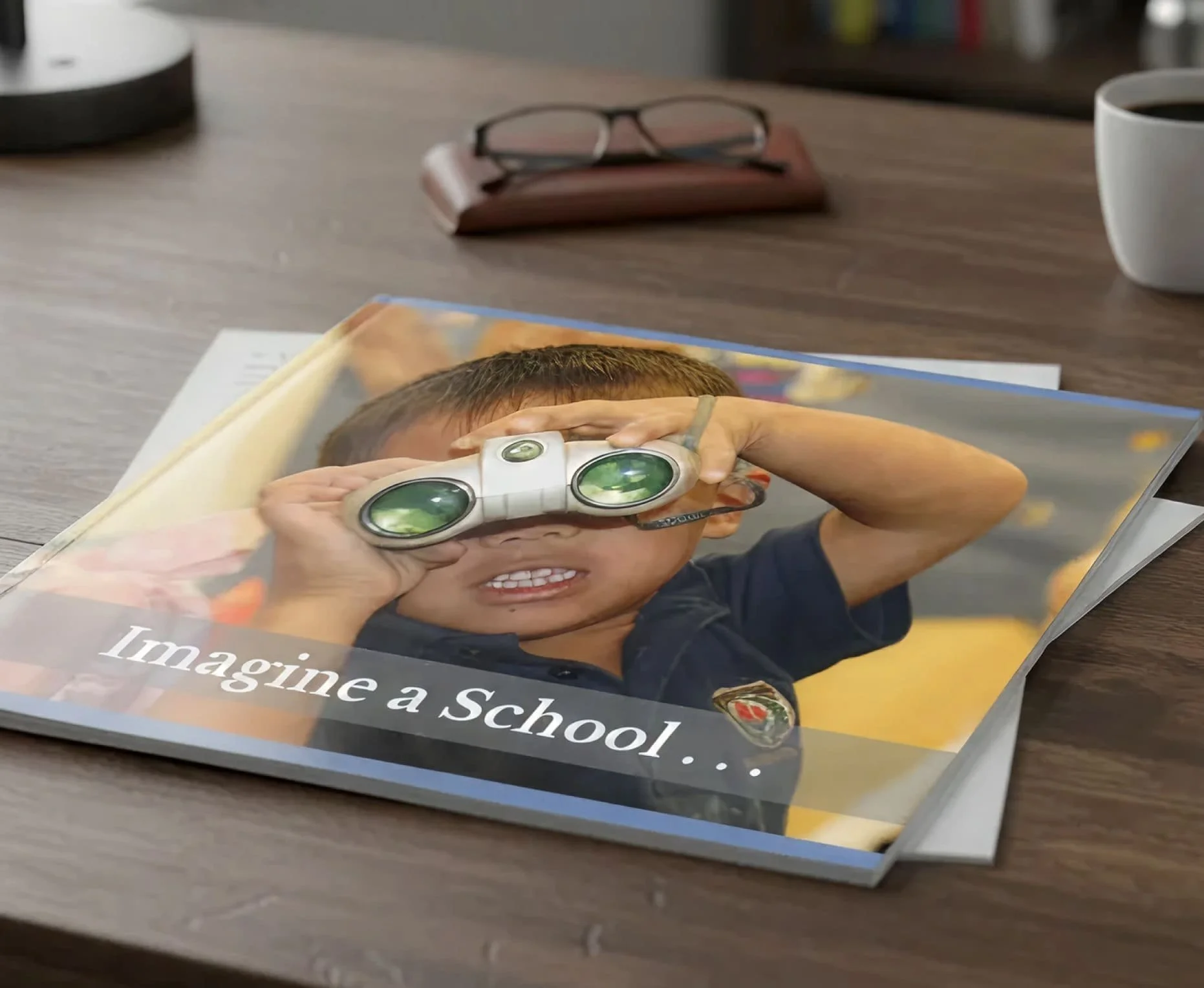 Close-up of a magazine page titled "Imagine a School." featuring a young boy with short hair and glasses holding a magnifying glass to his eye, smiling.