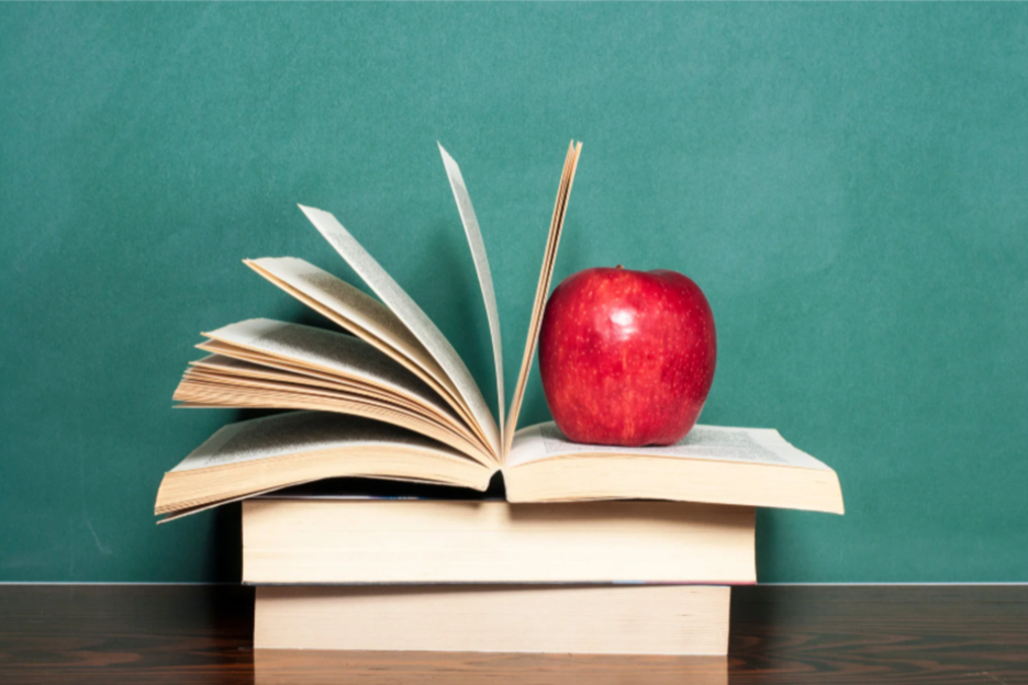 An open book with pages fanned out and an apple placed on top of it, set against a green background.