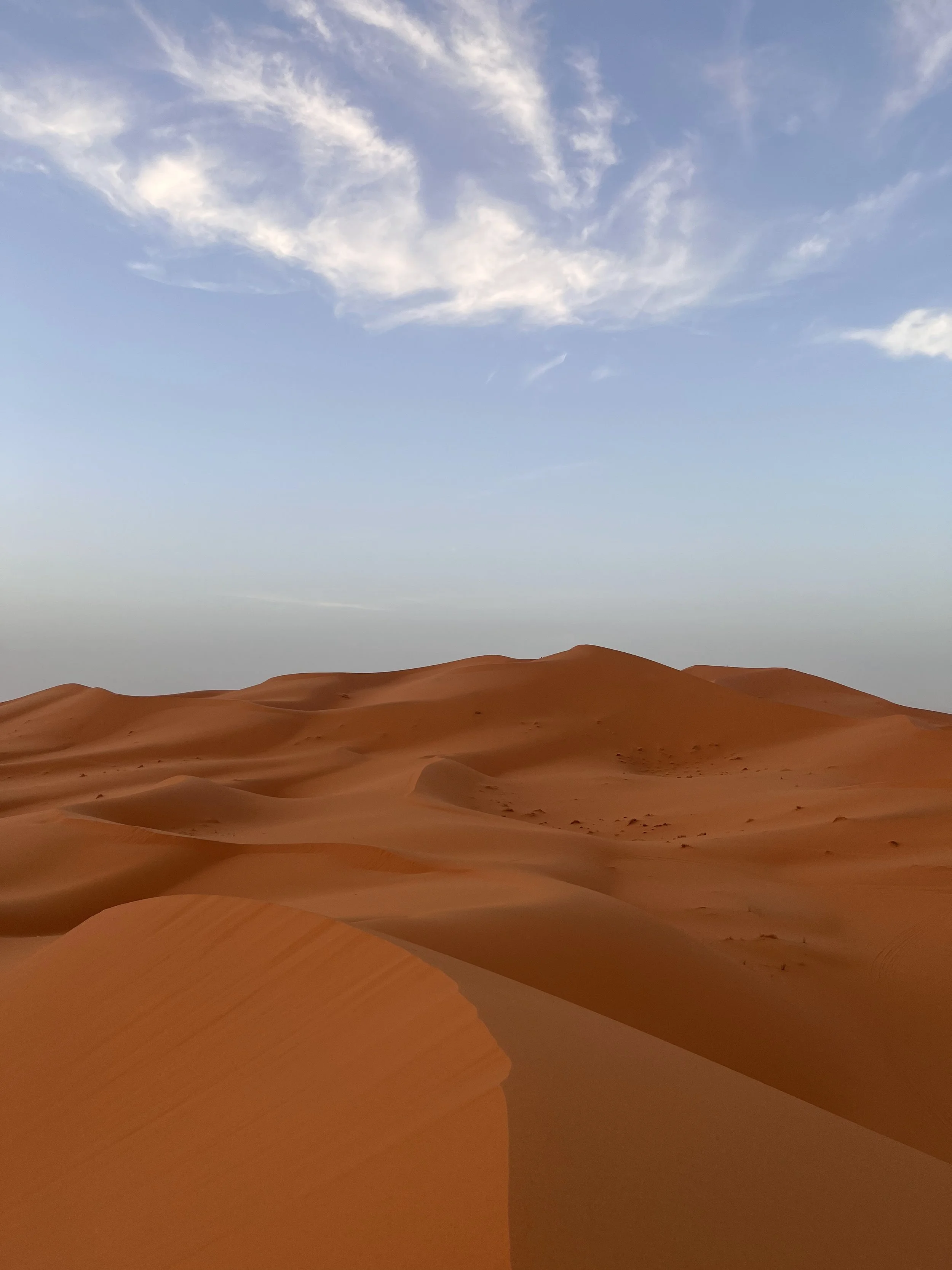 Sand dunes in a desert with a partly cloudy sky above.