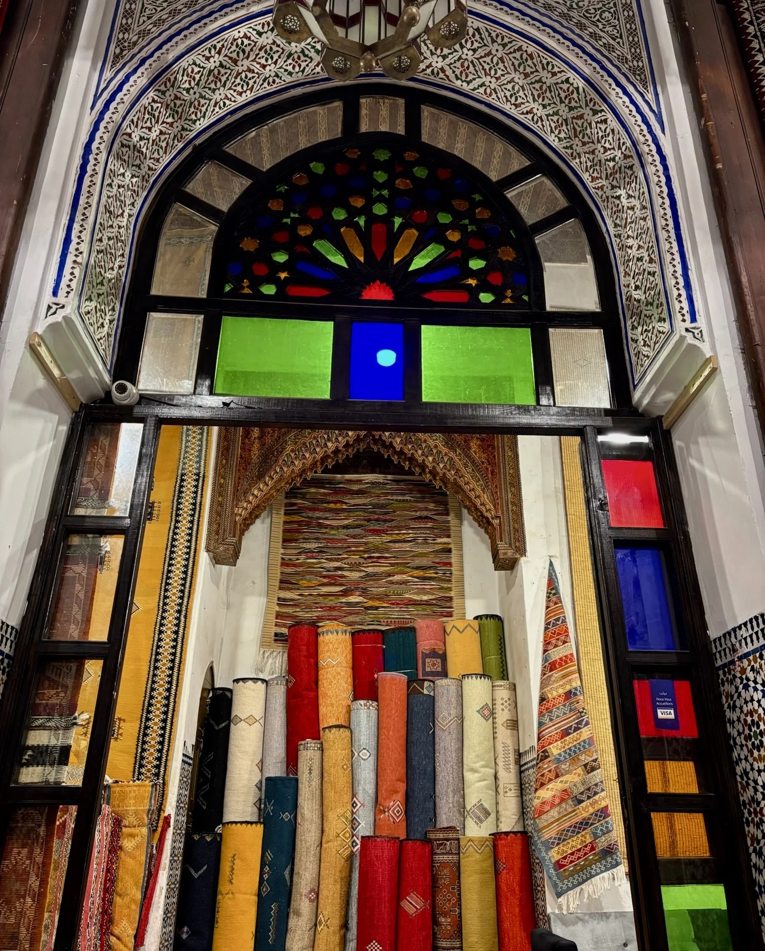 Traditional rug shop in Morocco, with colorful woven carpets displayed beneath an ornate arched window.