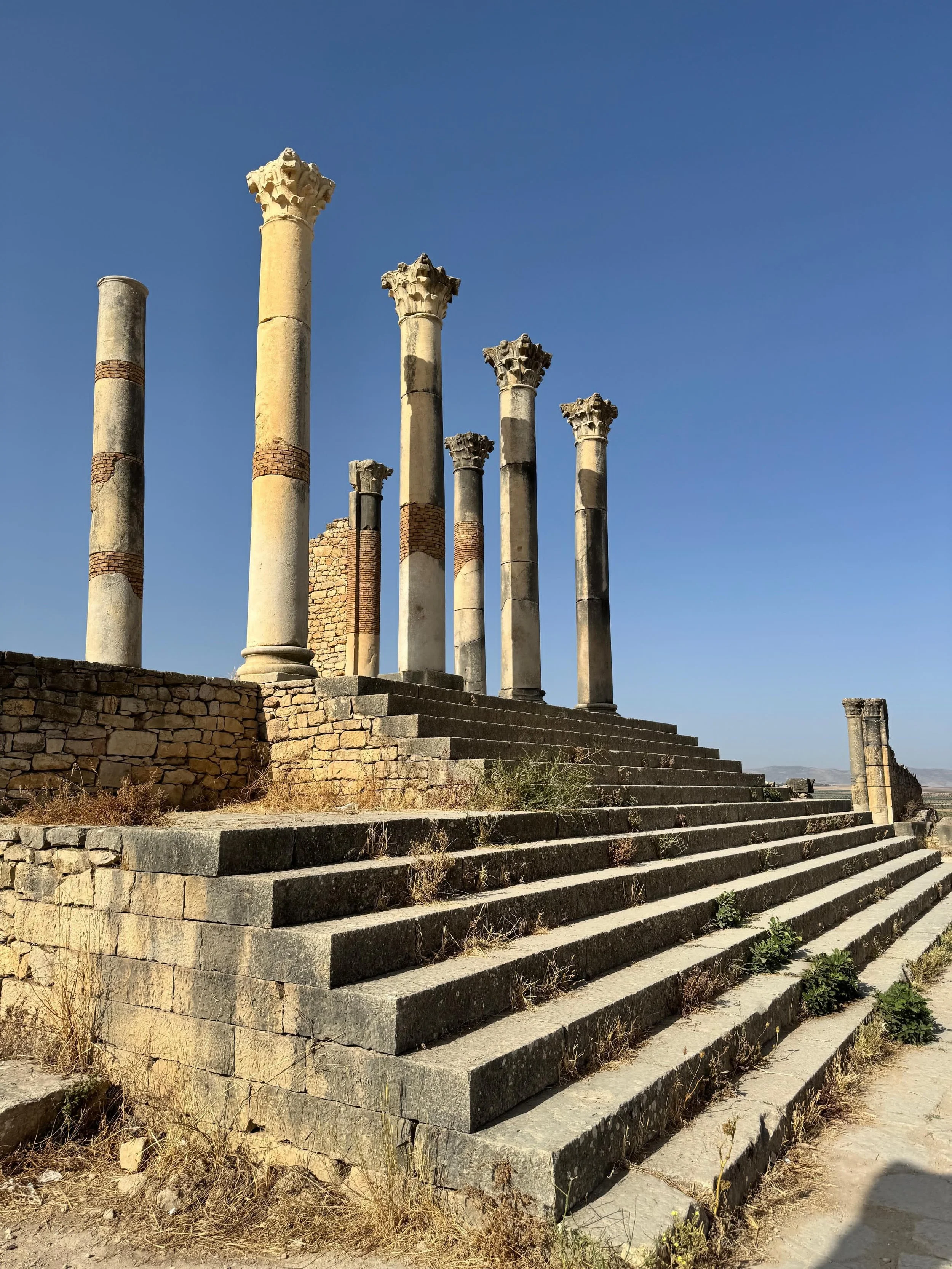 Ancient Roman ruins at Volubilis in Morocco, with stone columns and steps under a clear blue sky.