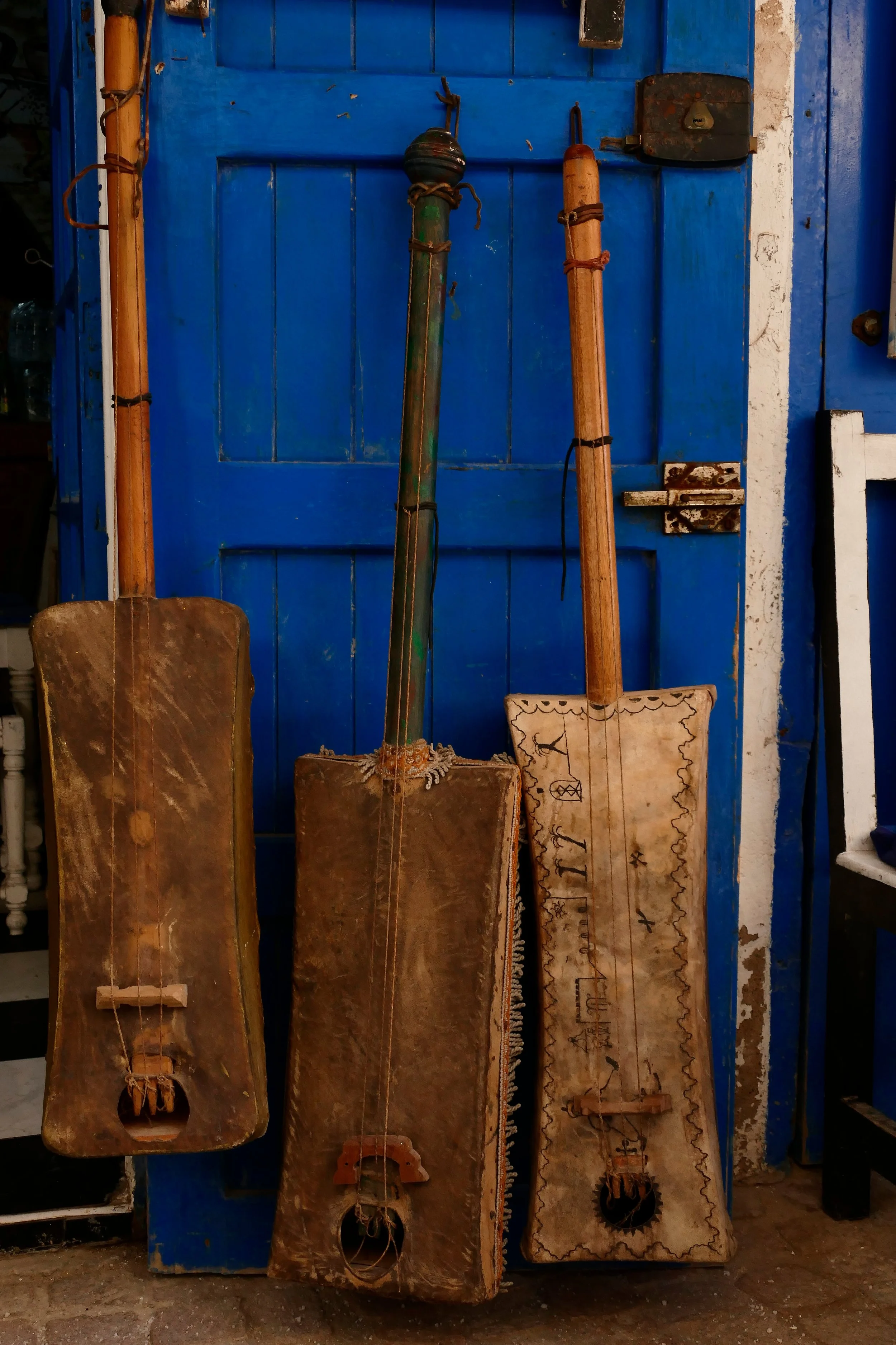 Three traditional wooden stringed instruments leaning against a bright blue door, with one having Mexican decorative designs.