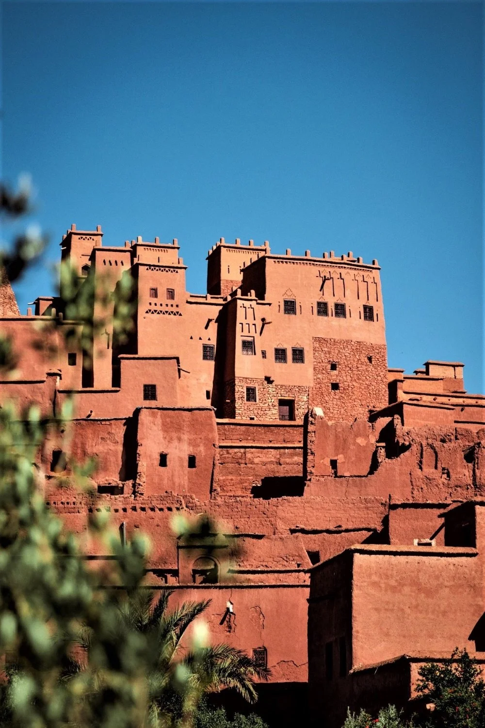 A historic mud-brick fortress or city built on a hill, with multiple levels and square towers, under a clear blue sky.