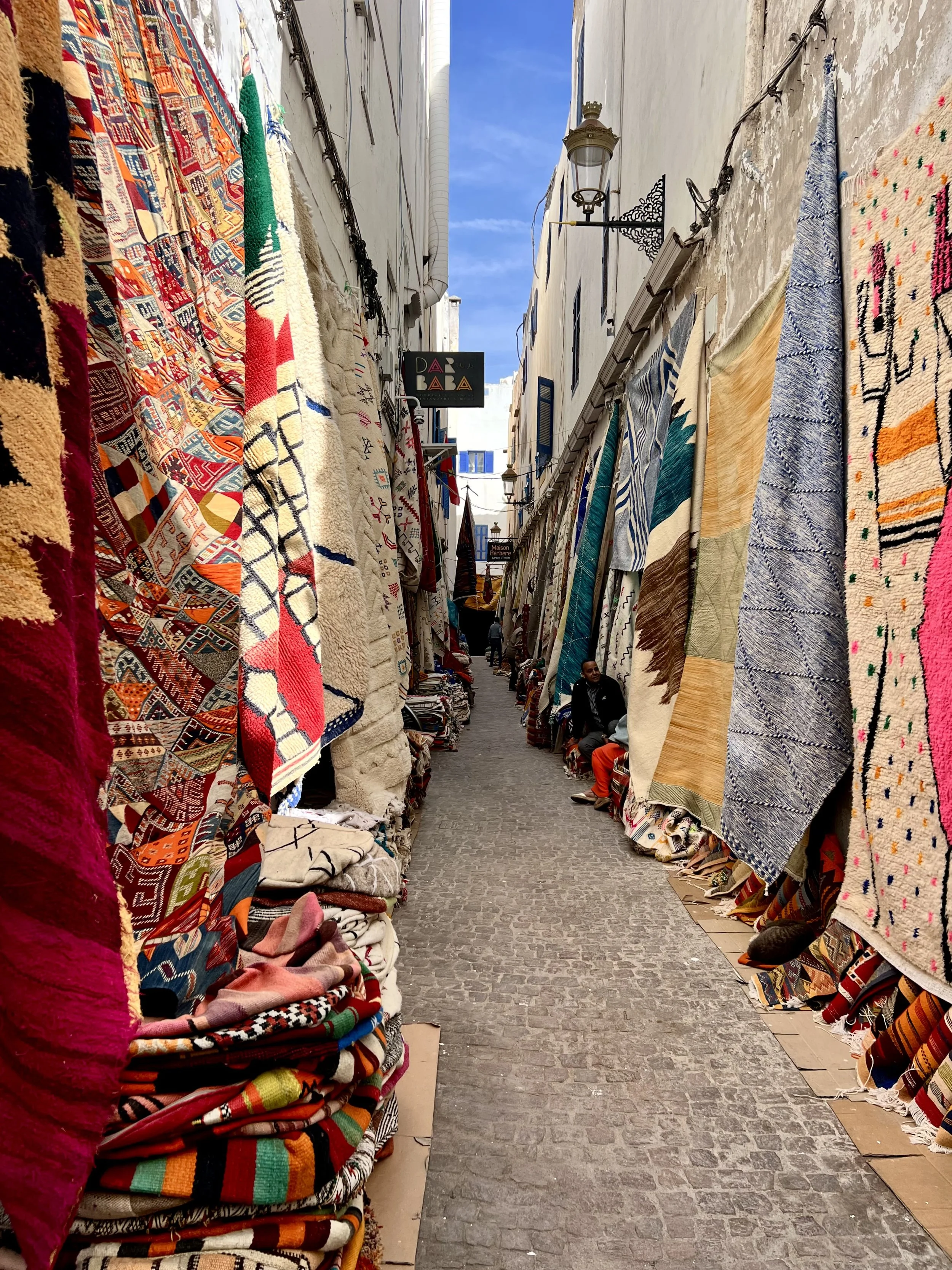 A narrow street lined with colorful, patterned rugs and carpets hanging on both sides.