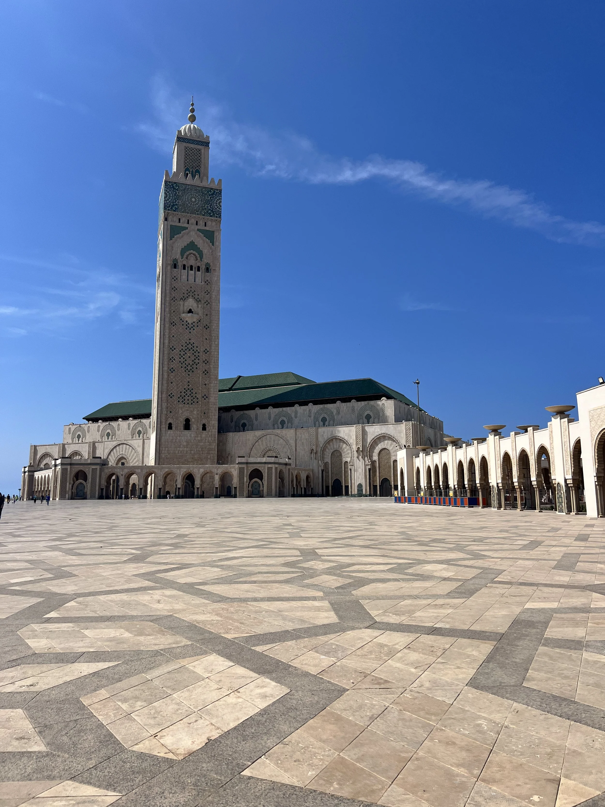 Large mosque with tall minaret and open courtyard, clear blue sky, and few people in the distance.