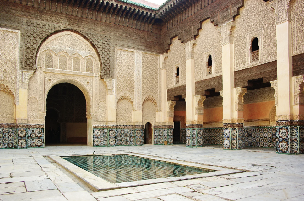 Ornate courtyard with carved arches, zellige tilework and a central reflecting pool at Ben Youssef Madrasa in Marrakech