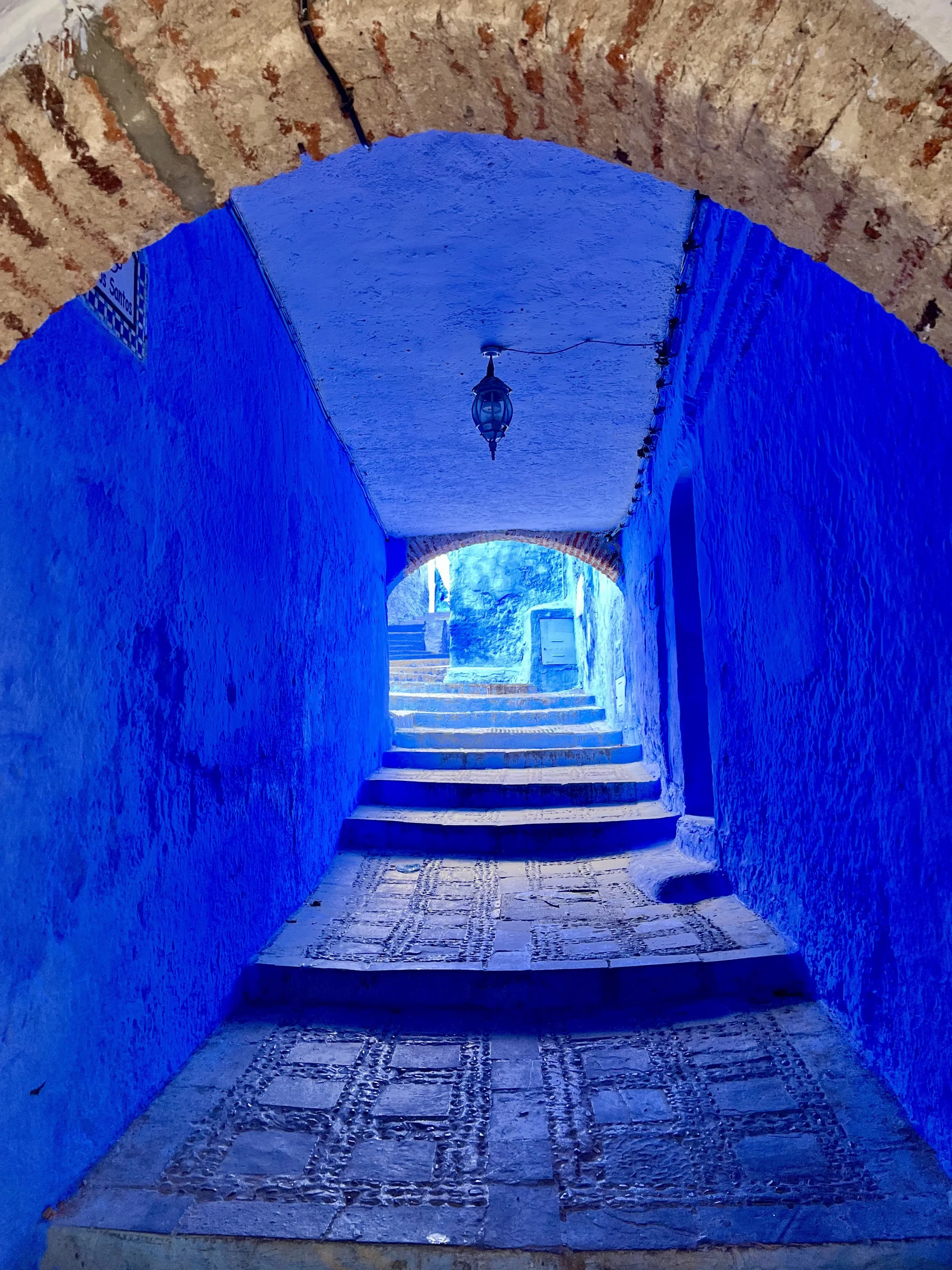 Blue-painted alleyway with stone steps and arched brick ceiling, lit by a hanging lantern.