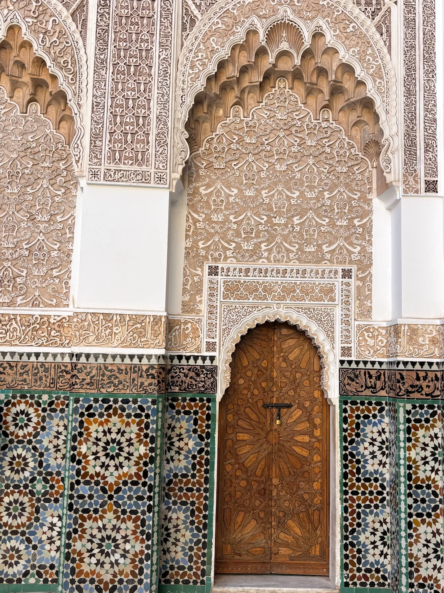 Intricate Moroccan-style architecture featuring a wooden door, decorative tiles, and ornate plasterwork.