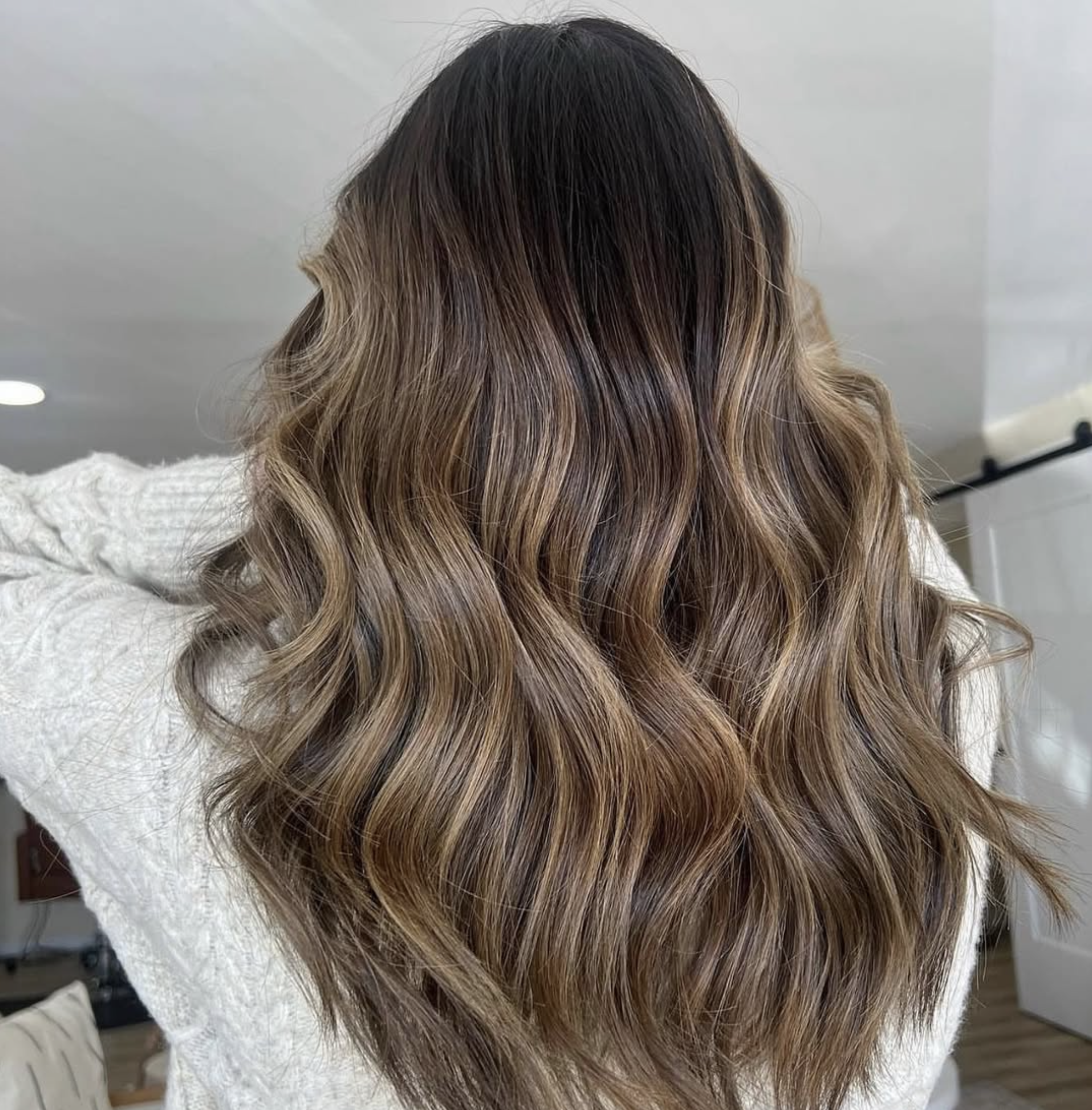 Back of a person's head with long, wavy, ombré hair that transitions from dark brown at the roots to lighter caramel towards the ends.