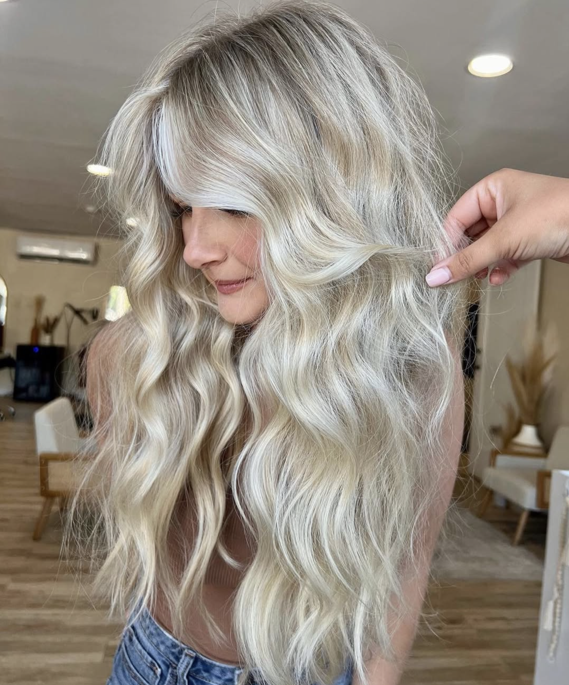 Woman with long, wavy, blonde hair, being styled or examined in a salon or home setting.