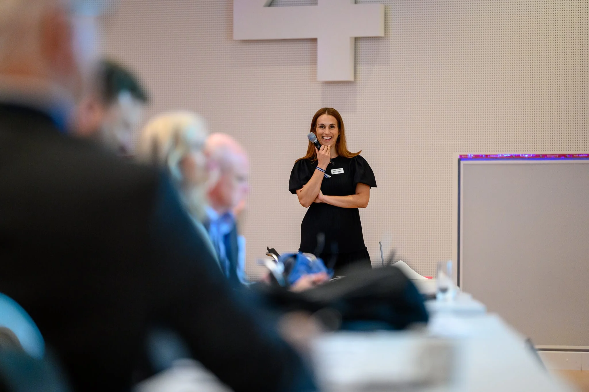 A woman holding a microphone and smiling in front of an audience in a conference room.
