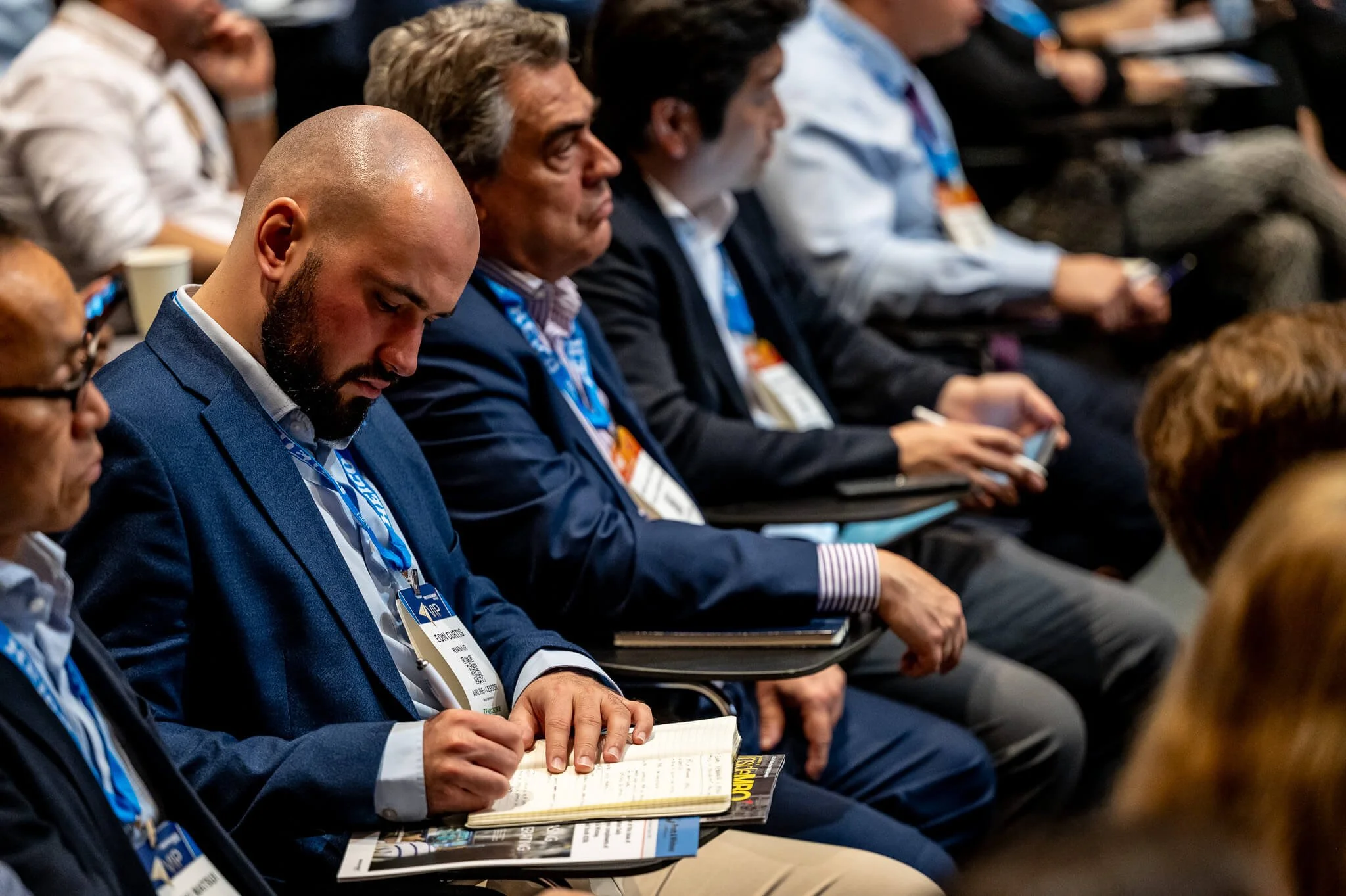 Business professionals seated in an auditorium, taking notes during a conference.