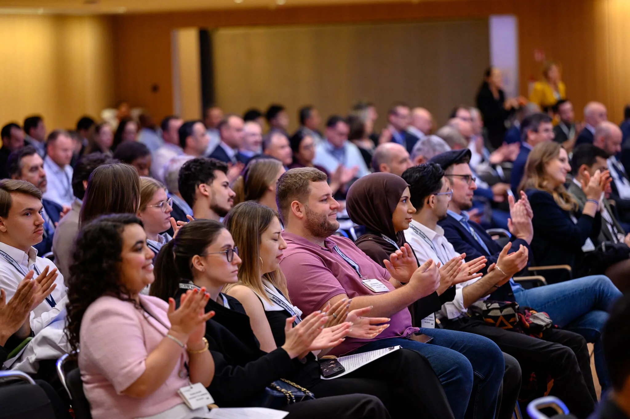 Audience sitting in a conference hall, clapping and paying attention to a presentation.