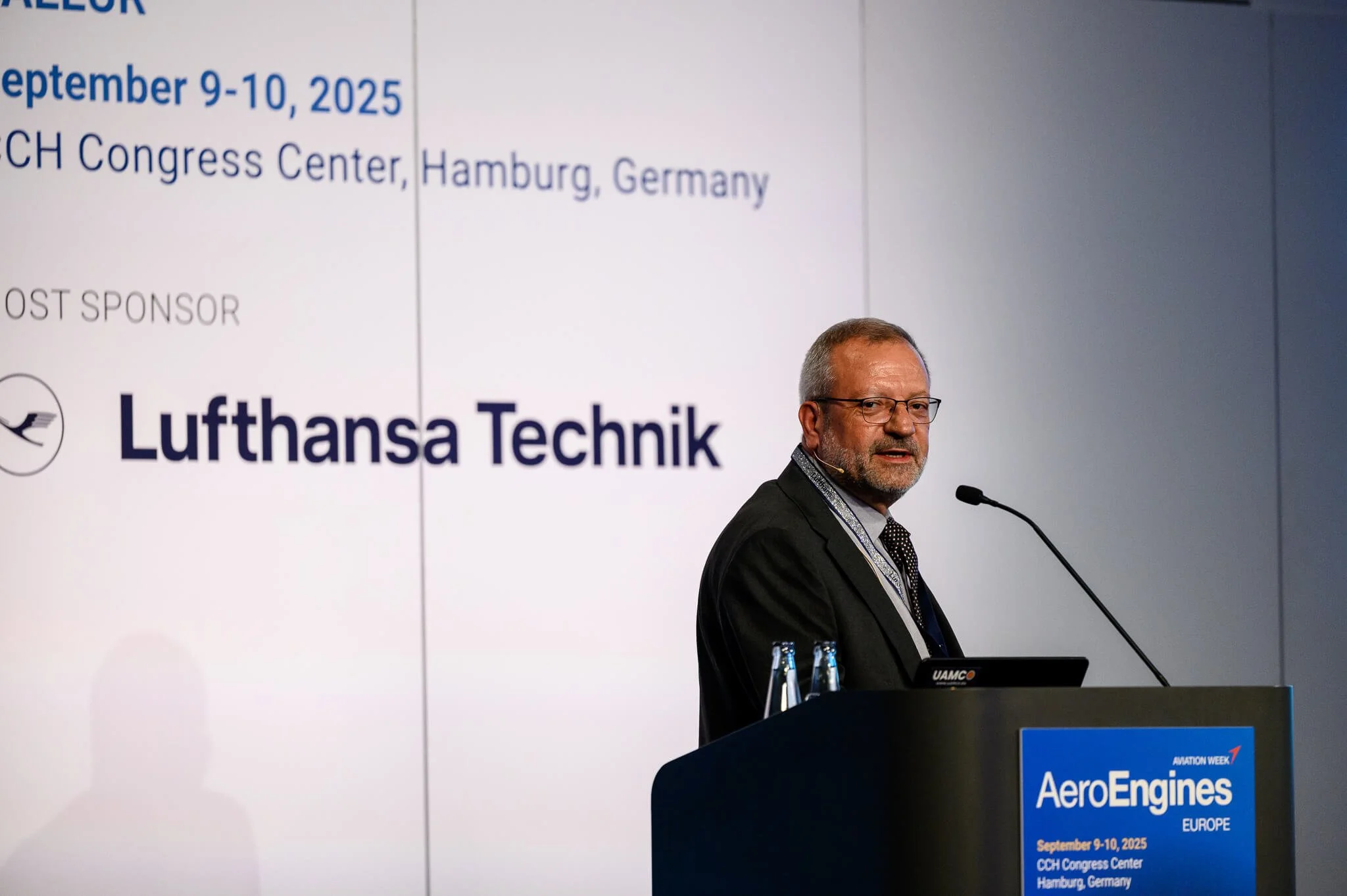 A man in glasses and a suit stands at a podium with a microphone, giving a presentation at AeroEngines Europe 2025 conference at CCH Congress Center in Hamburg, Germany, September 9-10, 2025.