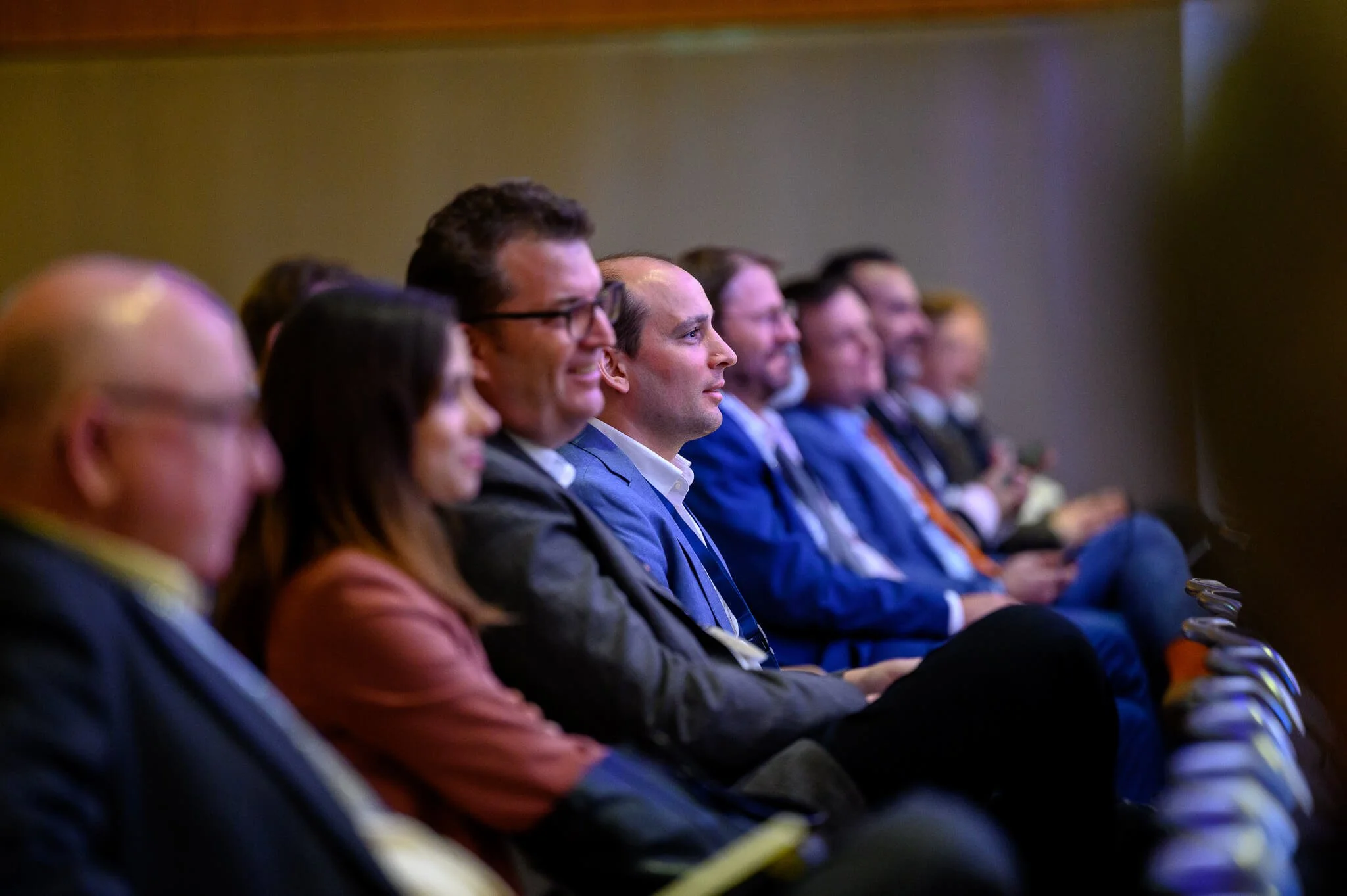 Audience of professionals seated in a conference or seminar, focused on a speaker or presentation.