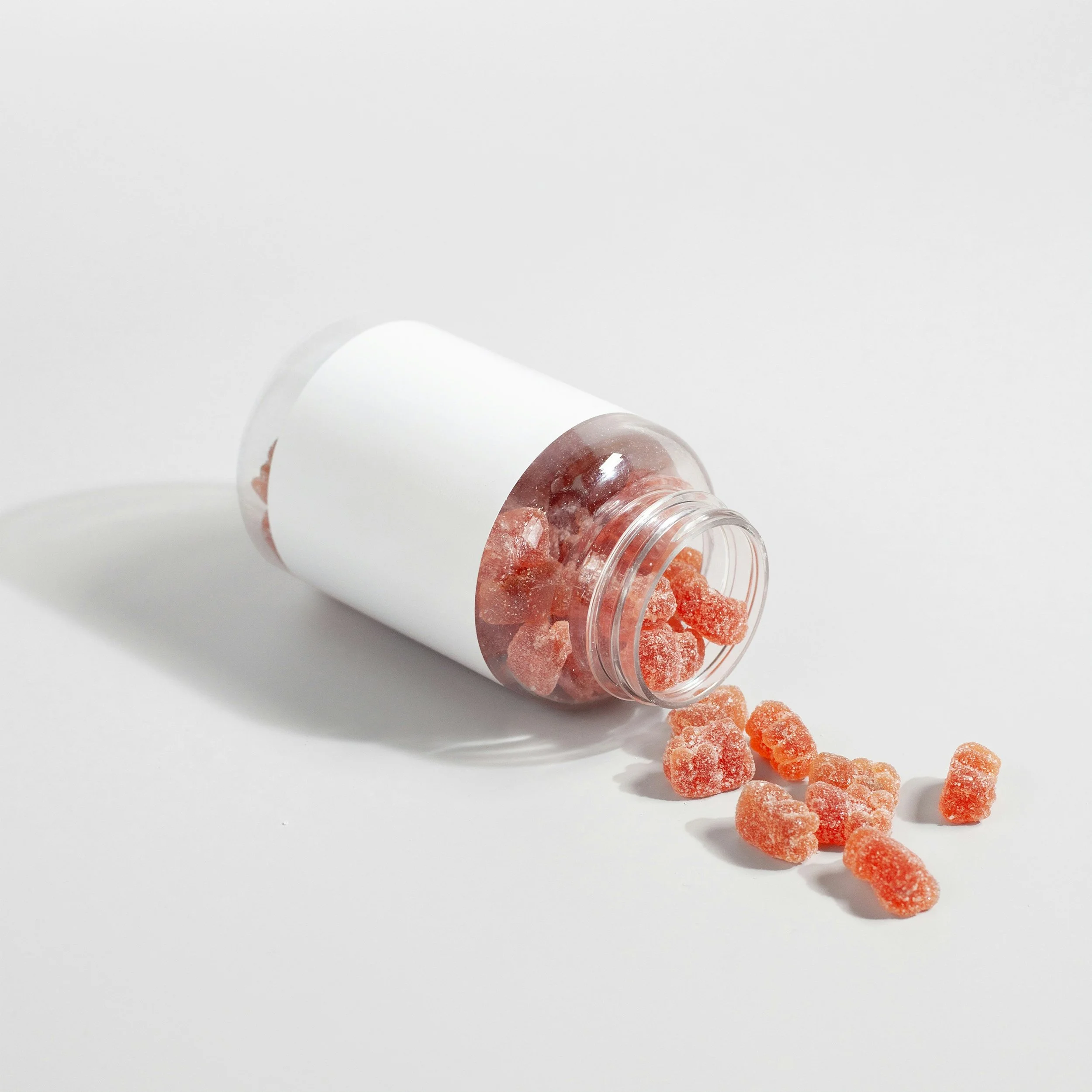 Orange gummy candies spilling out of a white container on a white surface.
