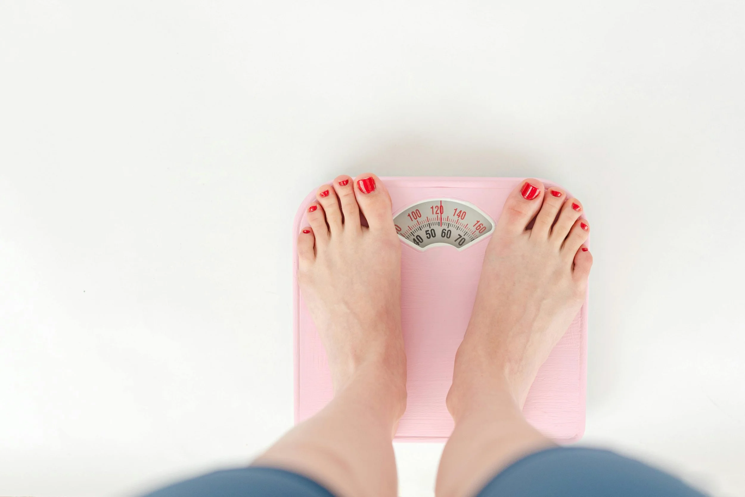 Person standing on a pink bathroom scale with red painted toenails, on a white background.