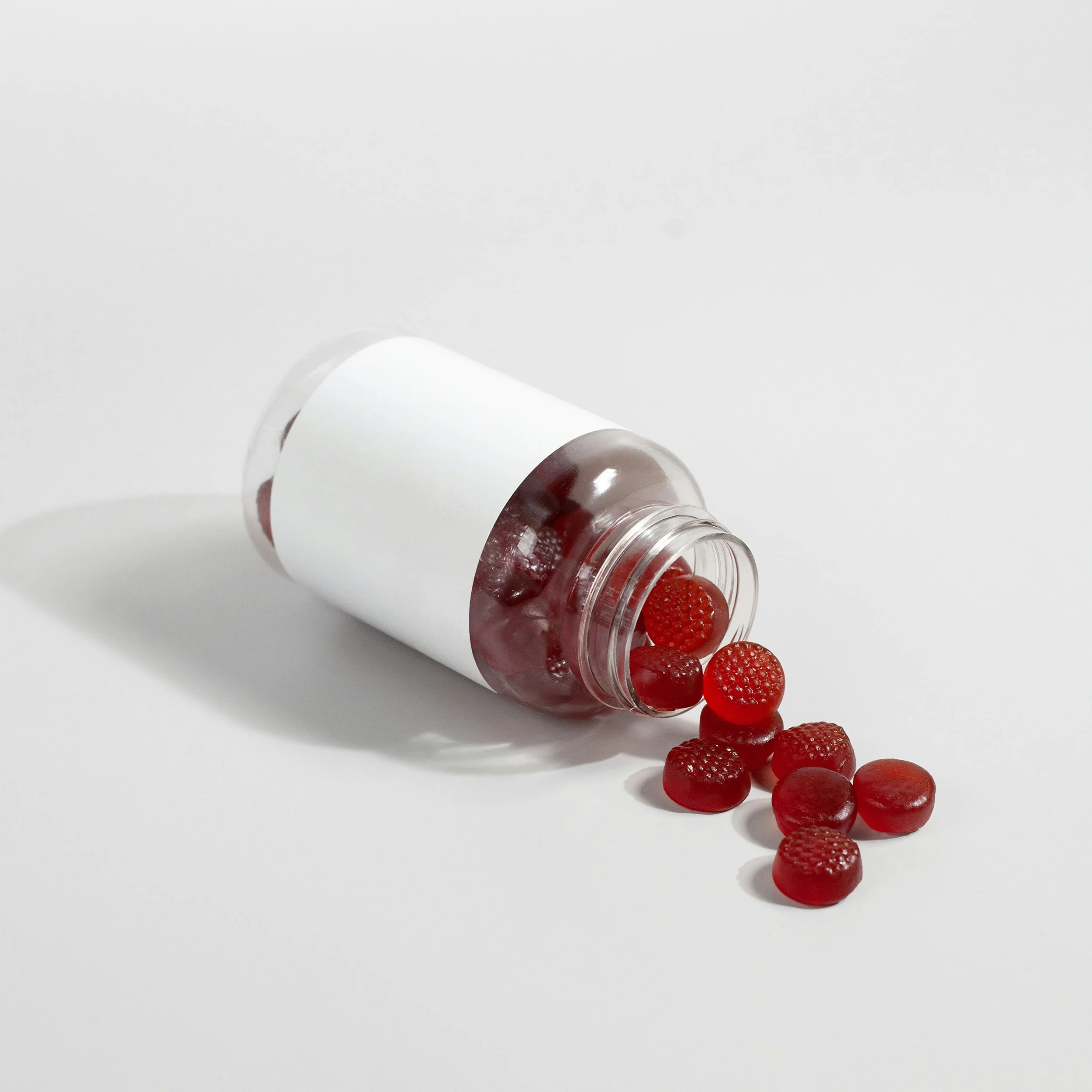 Red gummy candies spilling out of a white-labeled pill bottle on a white background.