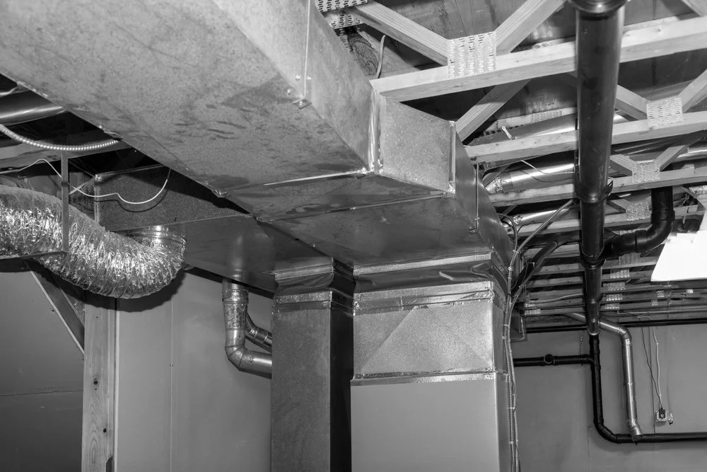 Ceiling ductwork and piping in a building's unfinished basement or utility area, featuring metal and insulated ducts.