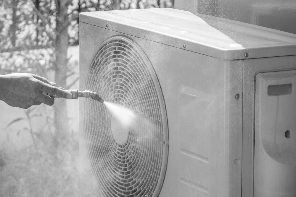 Person using a spray nozzle to clean an outdoor air conditioning unit.