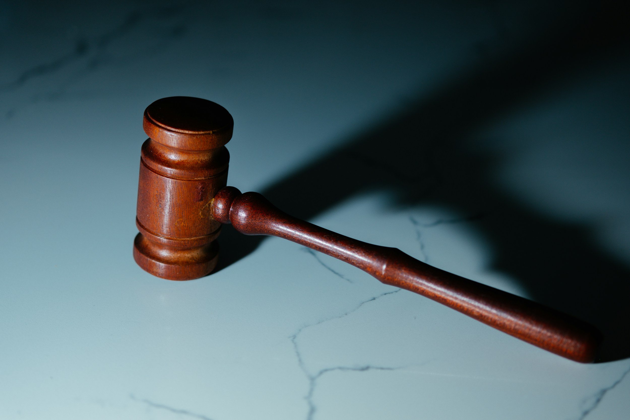 Wooden gavel resting on a light-colored marble surface with cracks, casting a shadow.