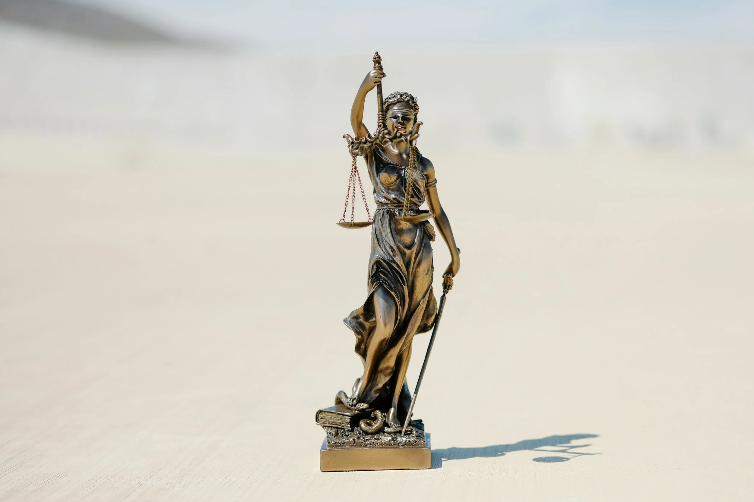 Brass Statue of Lady Justice with blindfold, scales, sword, and book, standing on a flat surface.
