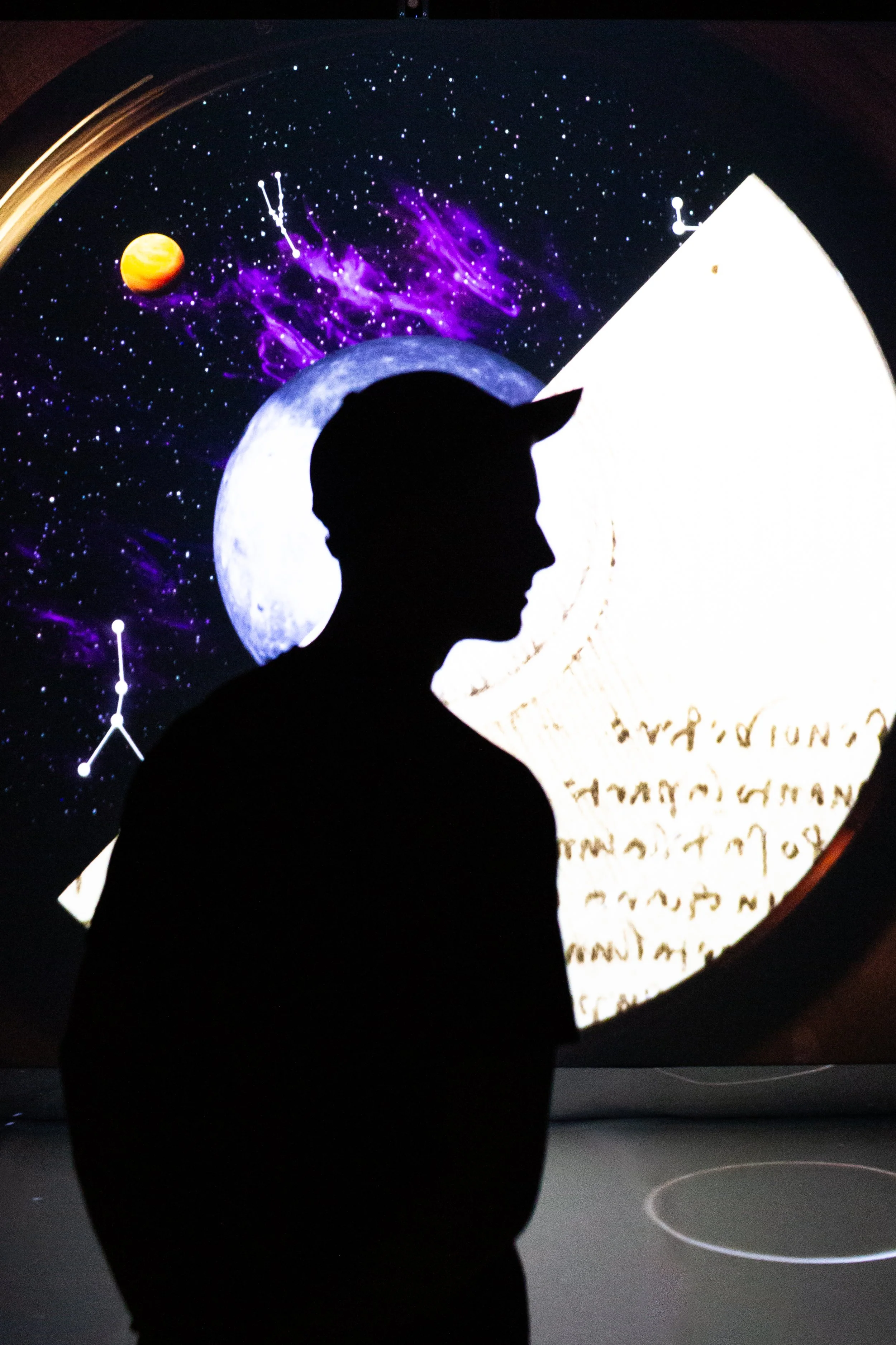 Silhouette of a person with cat ears in front of a space-themed digital display showing the moon, planets, stars, and constellations.