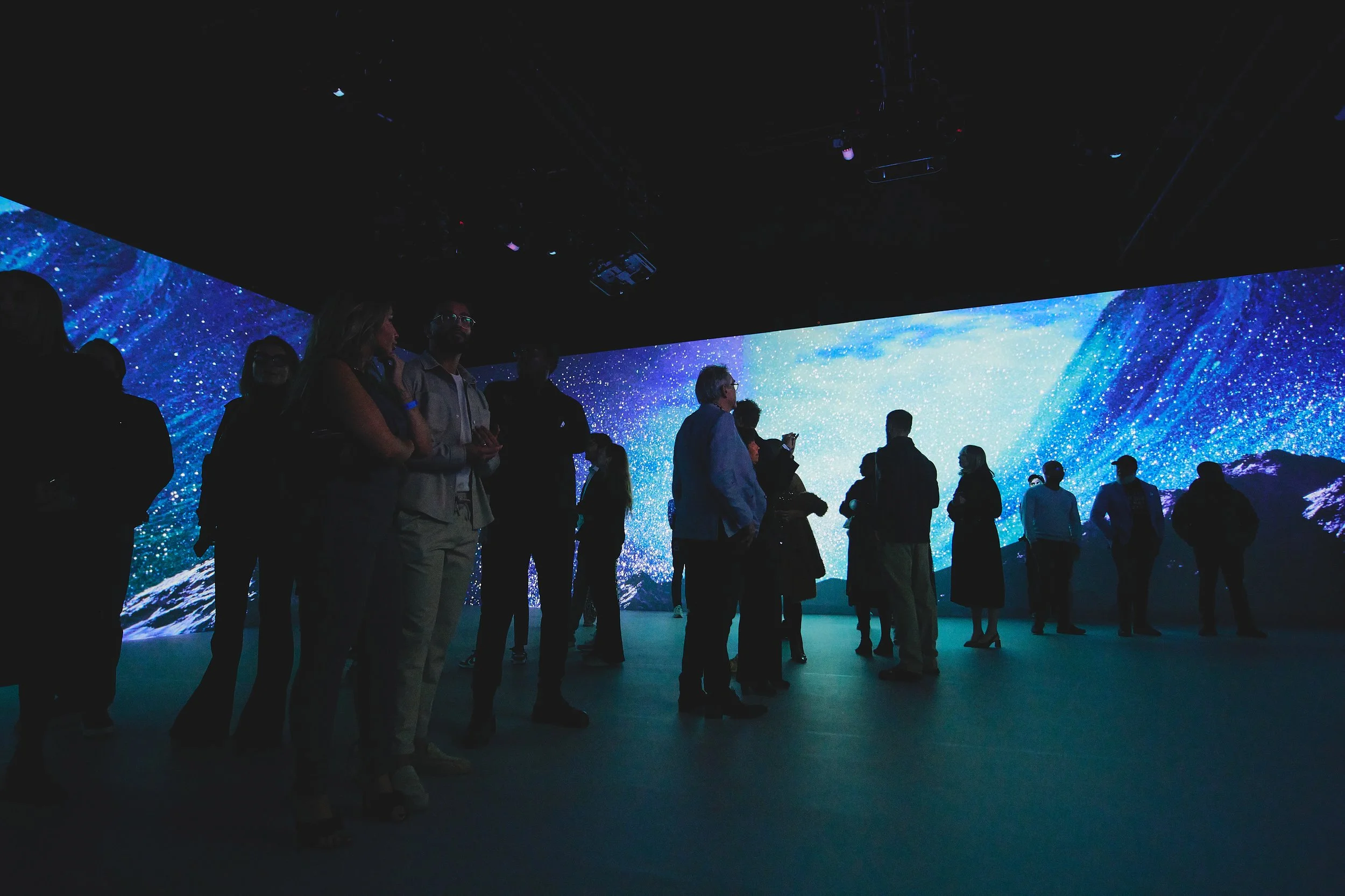 Group of people standing in front of a large digital display showing starry night sky and mountains.