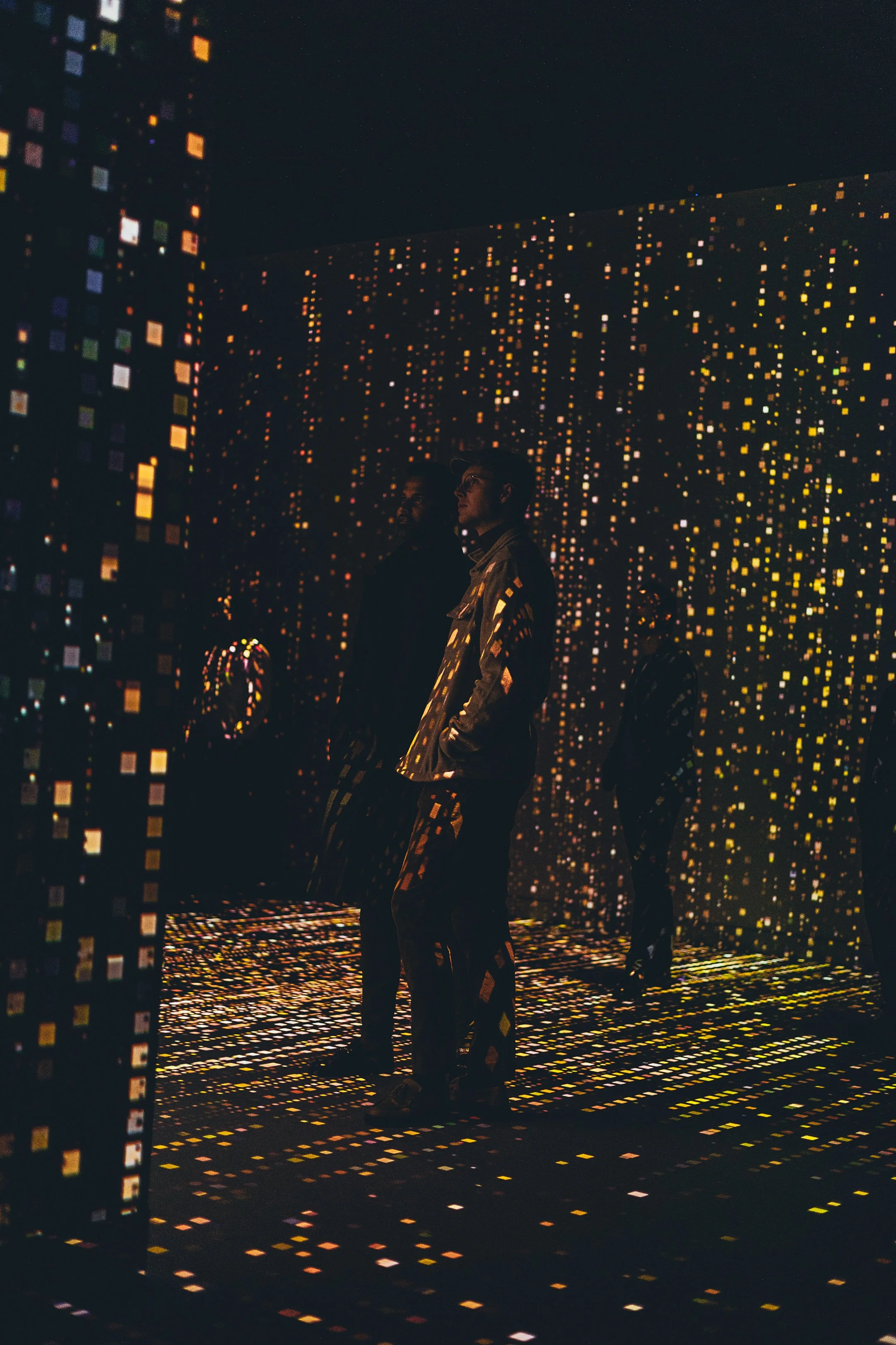 People inside an interactive digital art installation featuring walls and floor covered in colorful, glowing square pixels, creating an immersive and futuristic environment.