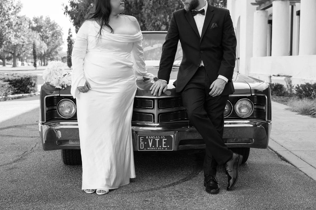 A bride and groom in wedding attire standing in front of a vintage car.