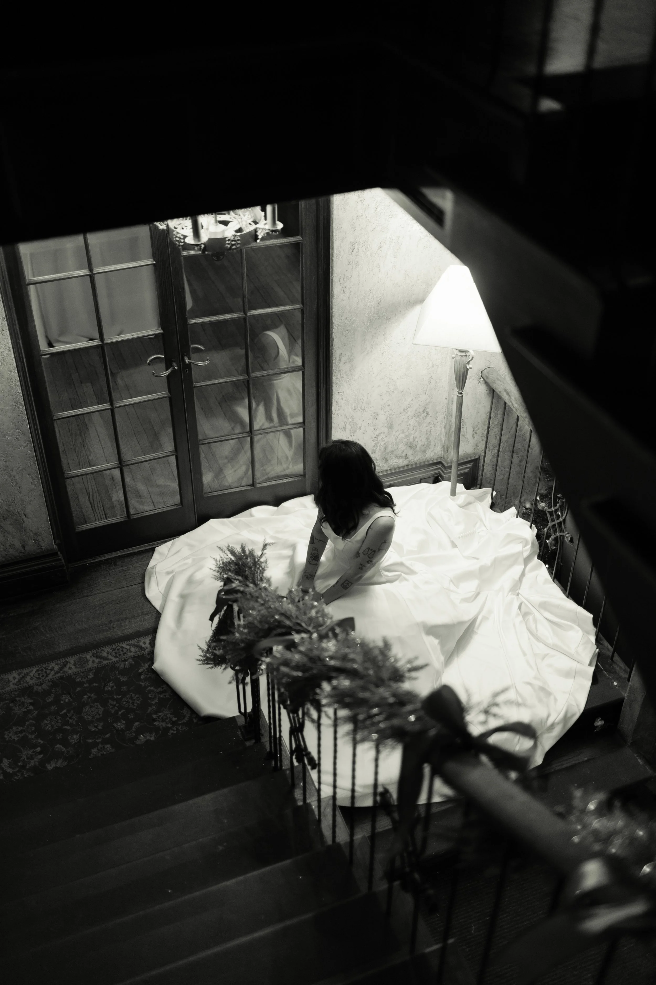A woman sitting on the ground in a dimly lit room, viewed from an overhead perspective, with a door and a lamp visible in the background.