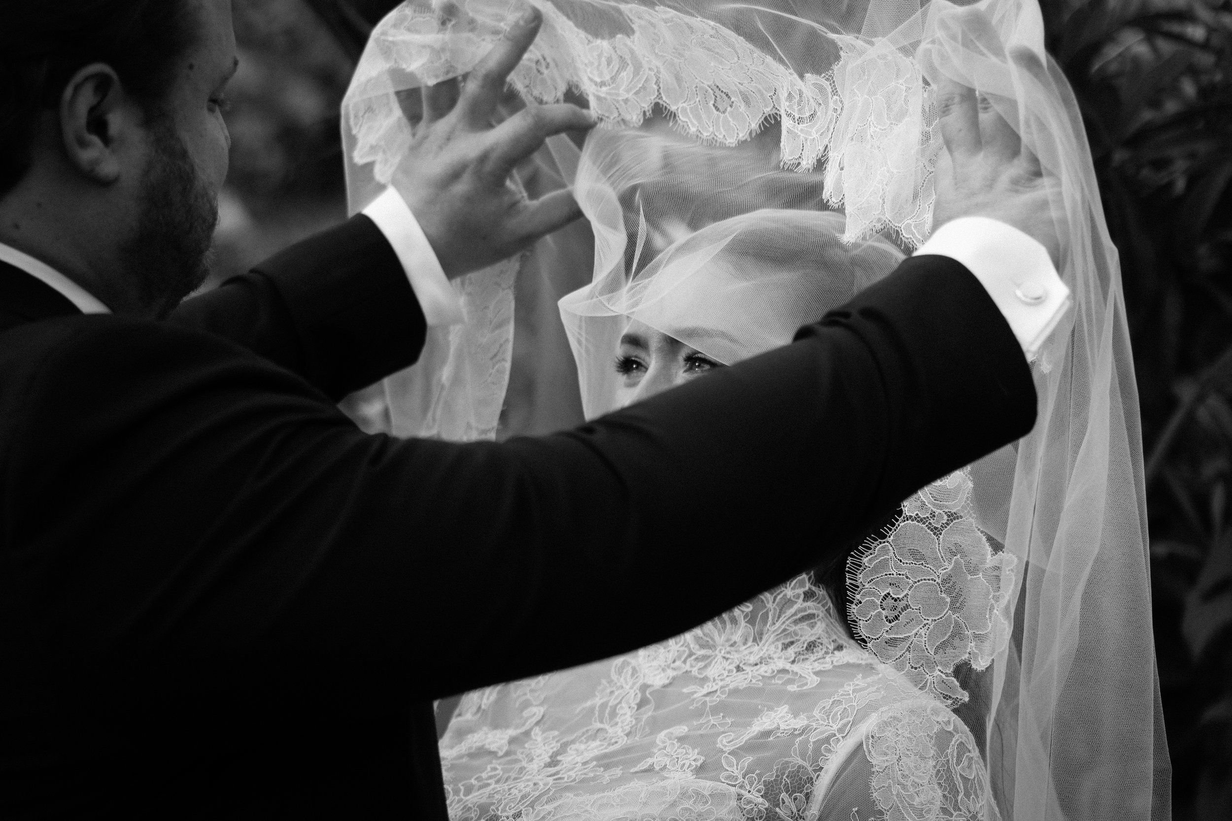 A black and white image of a man lifting a veil from a woman's face, the woman has tears in her eyes.